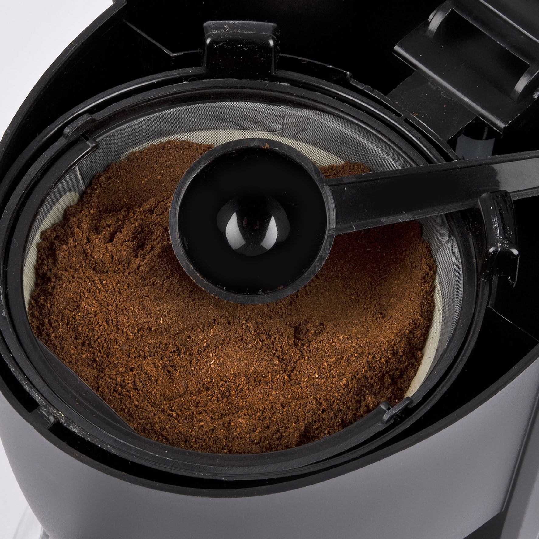 Kawa mielona w filtrze, z miarką, wewnątrz czarnego ekspresu do kawy.