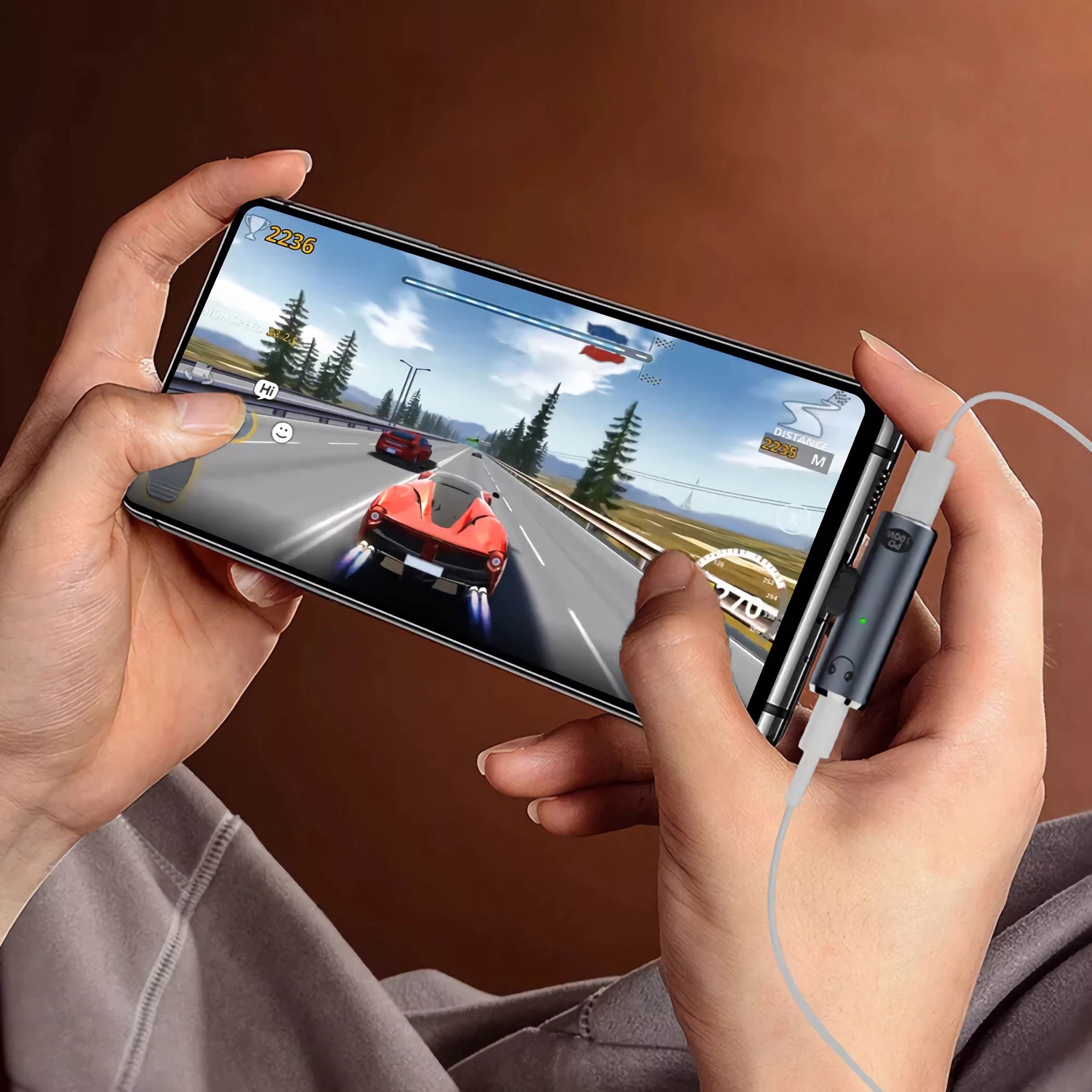 Hände halten ein Telefon, das ein Rennspiel spielt und an einen Adapter angeschlossen ist. Rotes Auto auf dem Bildschirm.