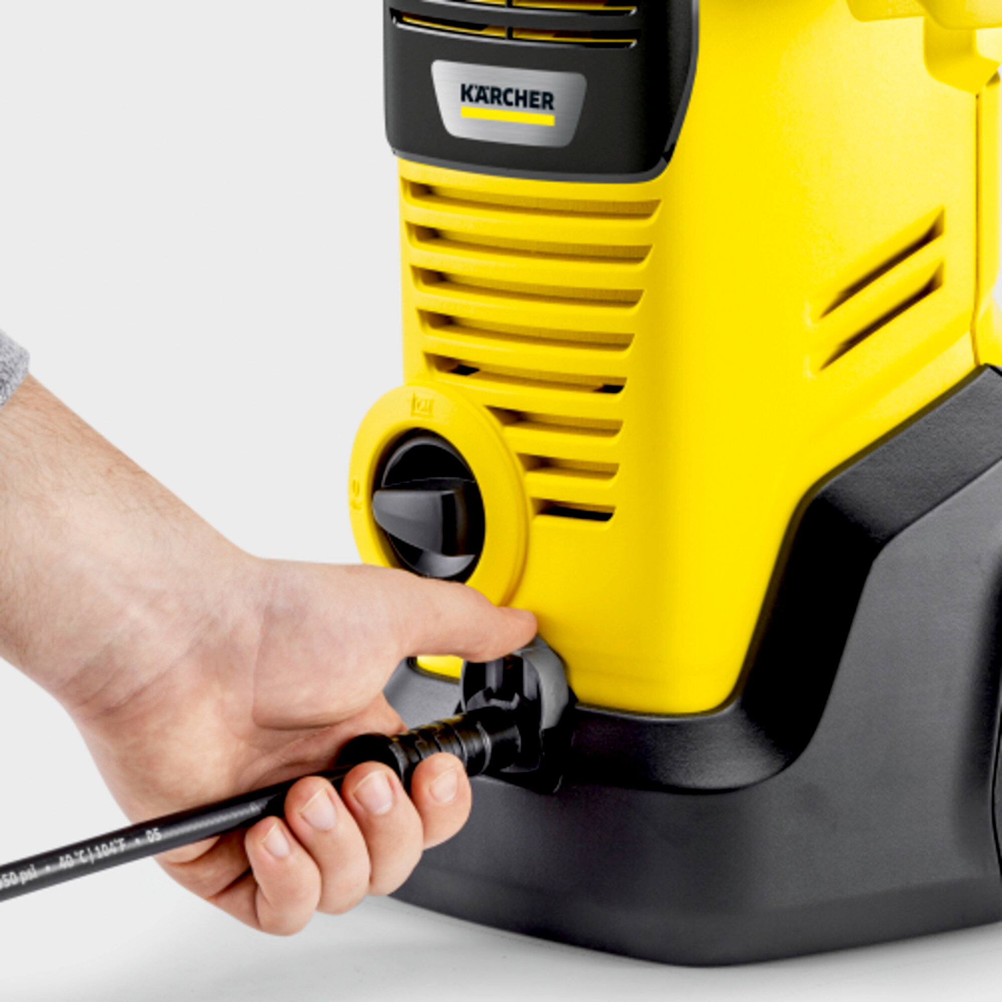 Eine Hand bedient einen schwarzen Schlauchanschluss an einem gelb-schwarzen Karcher-Hochdruckreiniger.
