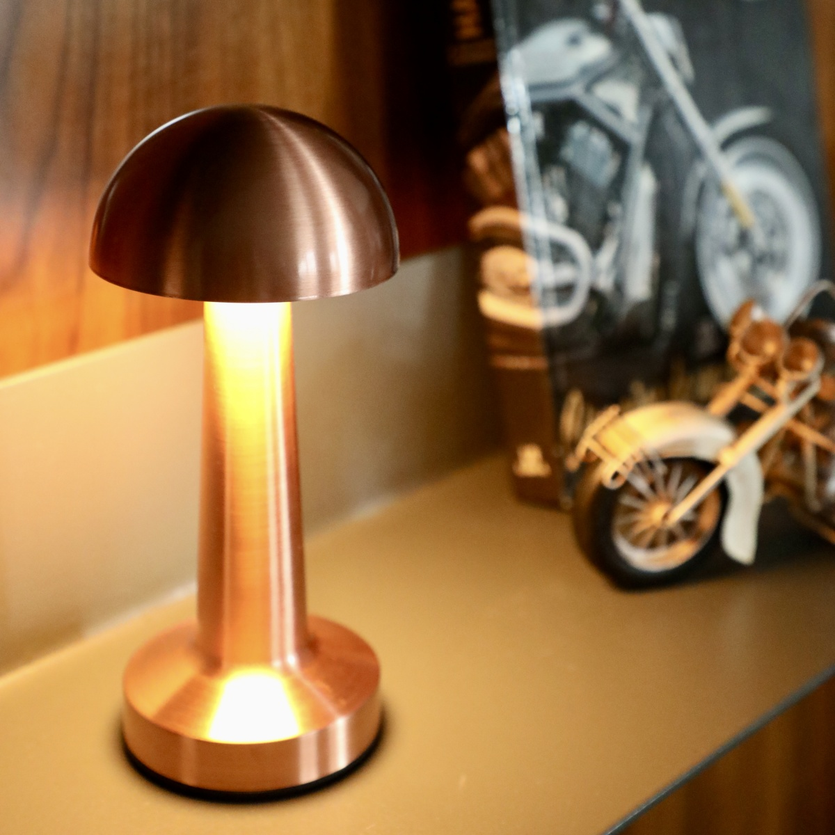 Lámpara color cobre con imagen de moto al fondo sobre una estantería.