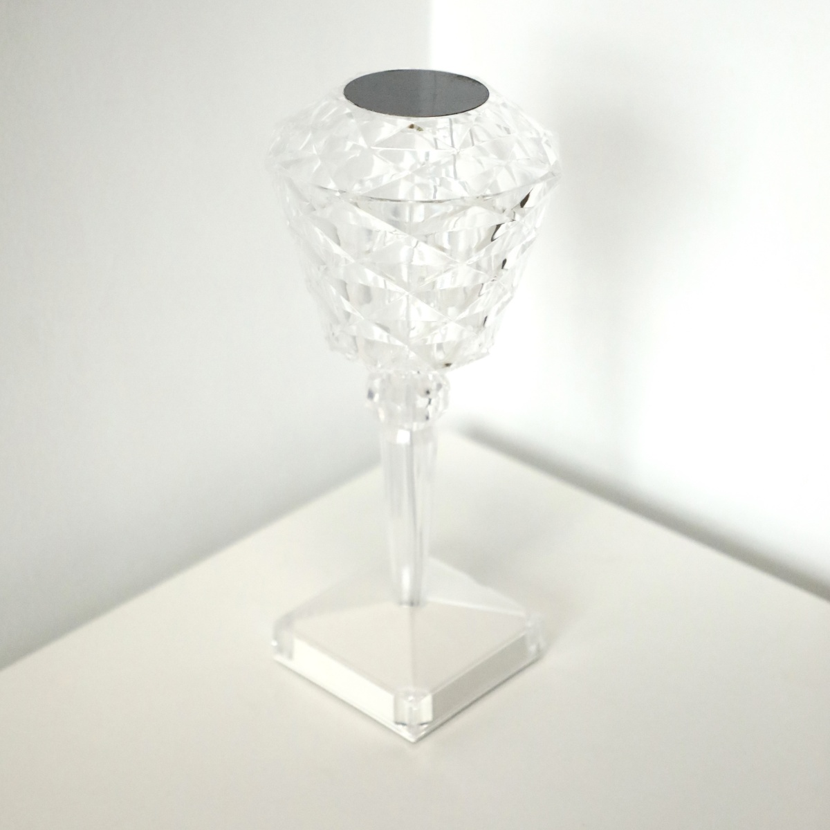 Lámpara de cristal sobre superficie blanca. Diseño de corte de diamante. Base minimalista. Fondo: pared blanca.