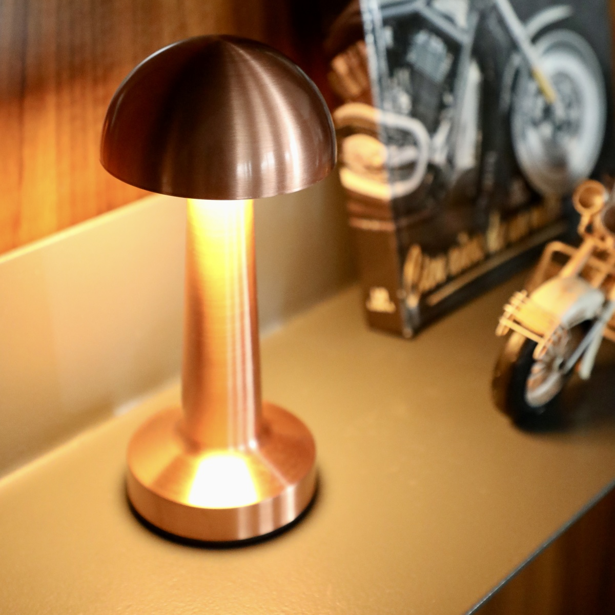 Lámpara de mesa de cobre. Un modelo de motocicleta y una revista en el fondo.