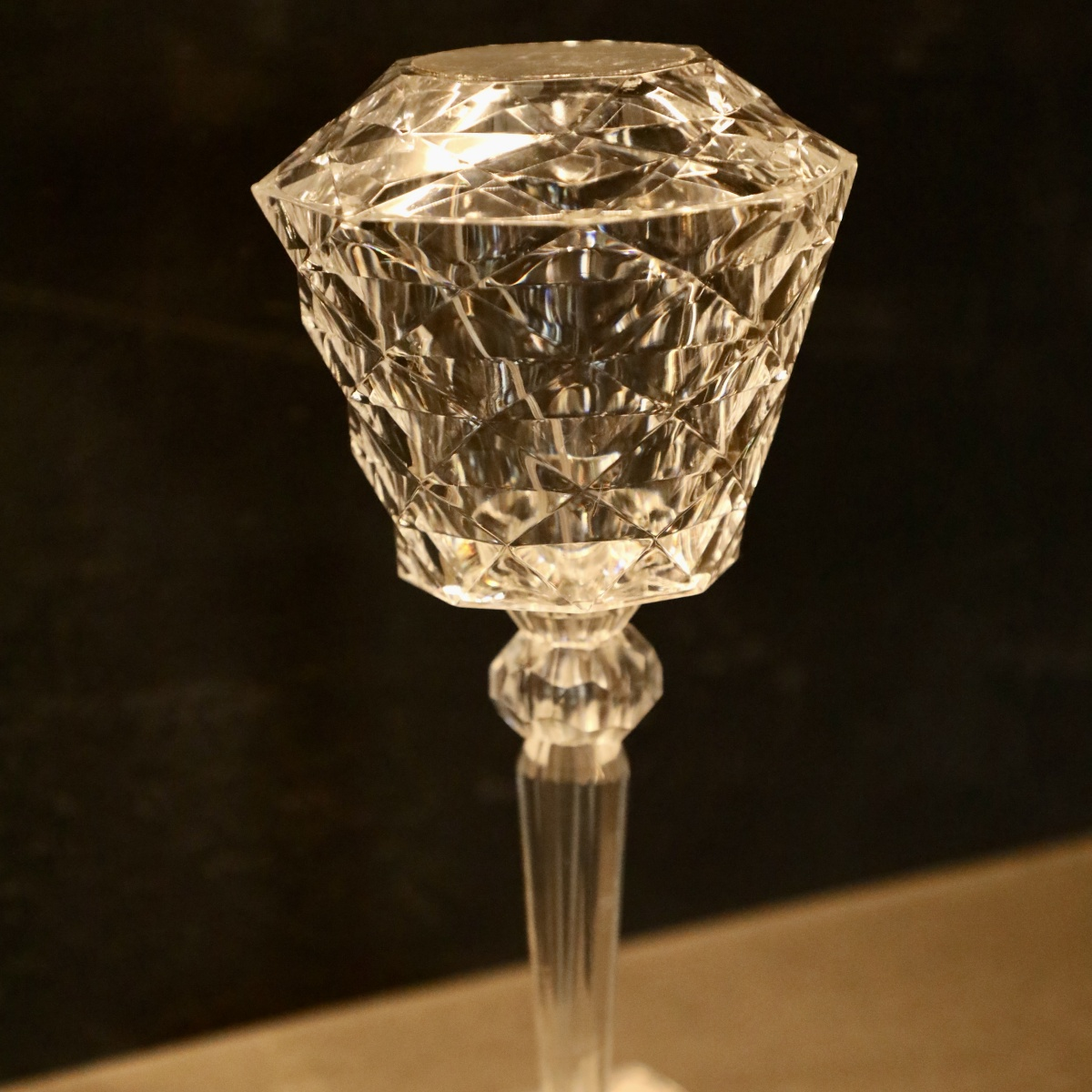 Un candelabro de cristal transparente tallado en diamante sobre un fondo oscuro, mostrando refracción de luz.