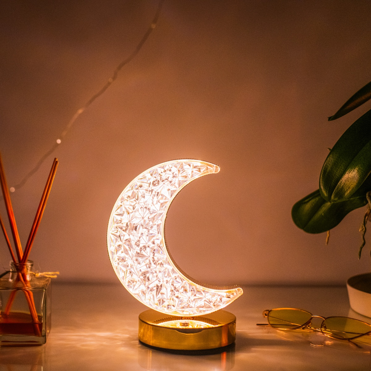 Lámpara decorativa con forma de luna. Base dorada con media luna iluminada, cristalina y luz cálida.