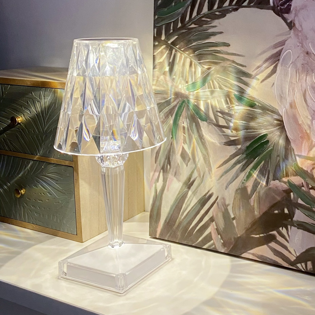 Lámpara de cristal transparente sobre una superficie blanca. Fondo con pintura y cajón de madera.