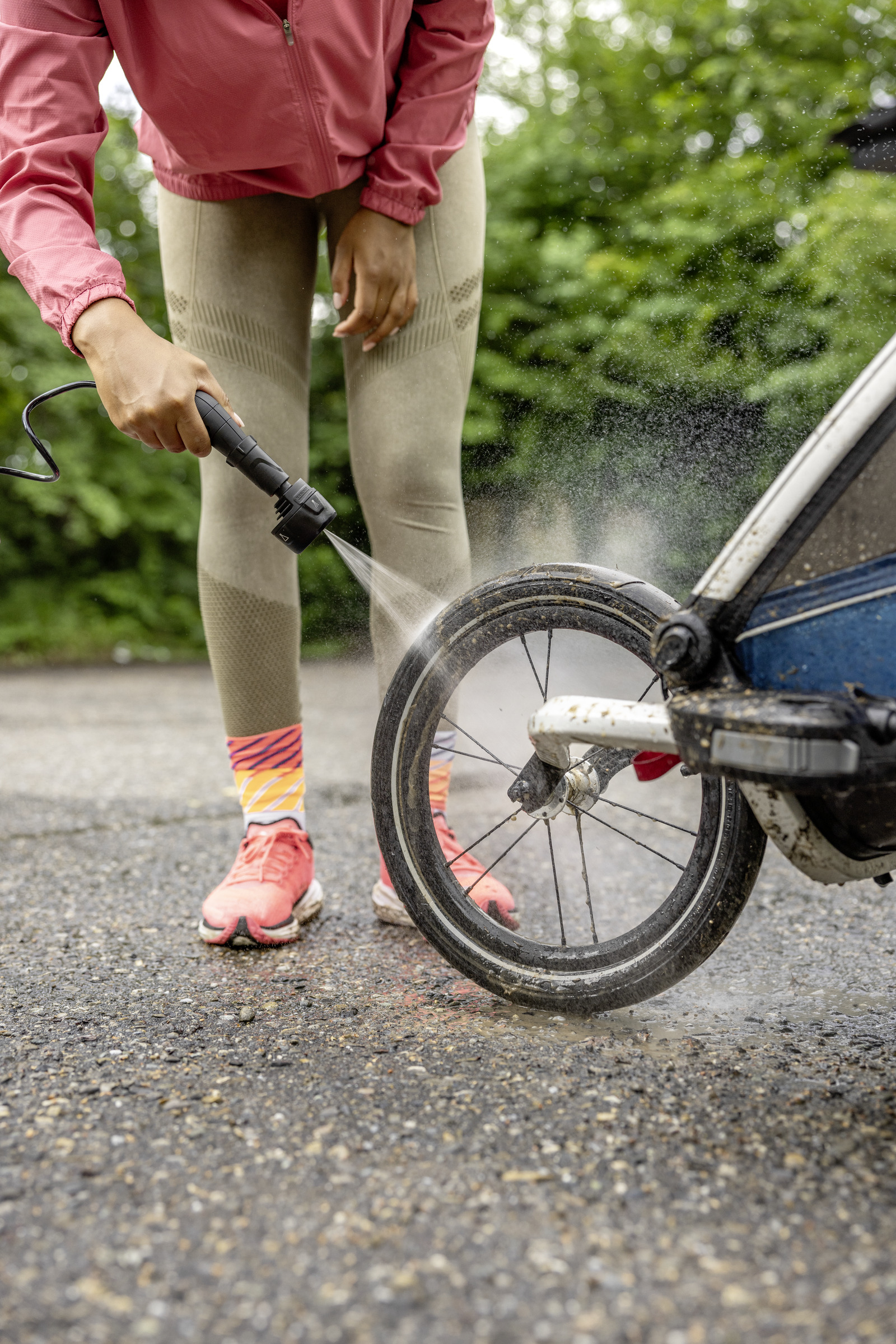 Woman cleaning a baby stroller wheel with a pressure washer.