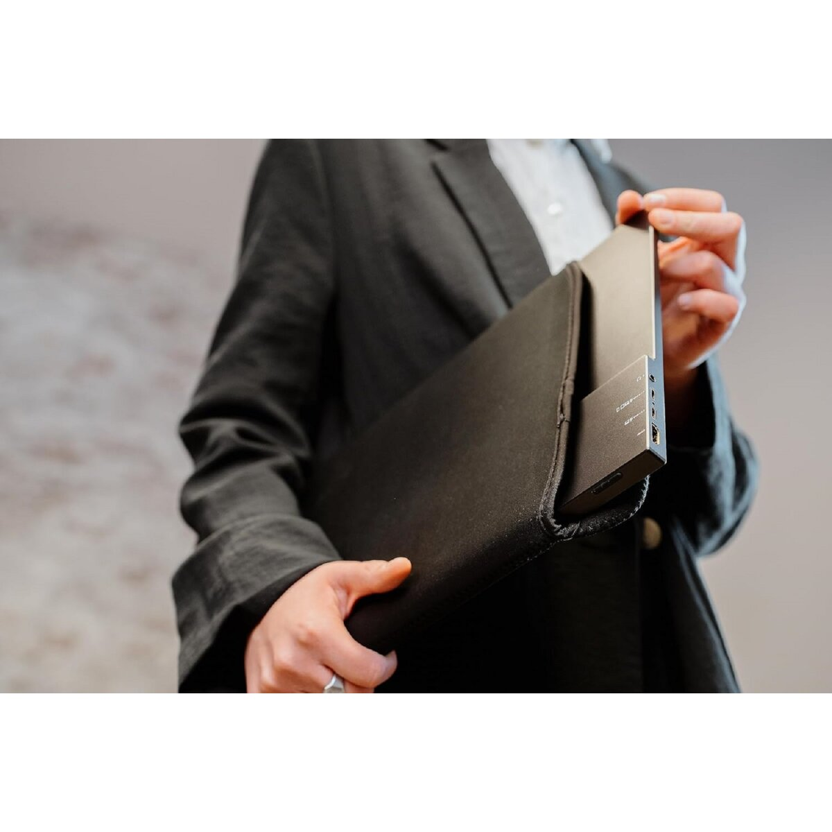 Osoba trzyma czarne etui, częściowo zasłaniając zawartość. Widoczne urządzenie z portami.