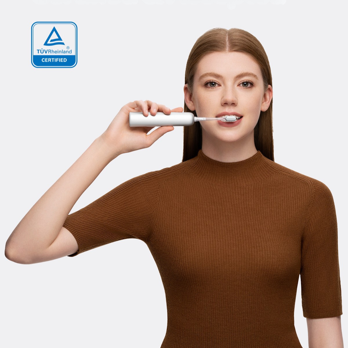 Kobieta trzymająca białą elektryczną szczoteczkę do zębów. Pokazuje zęby. Białe tło.