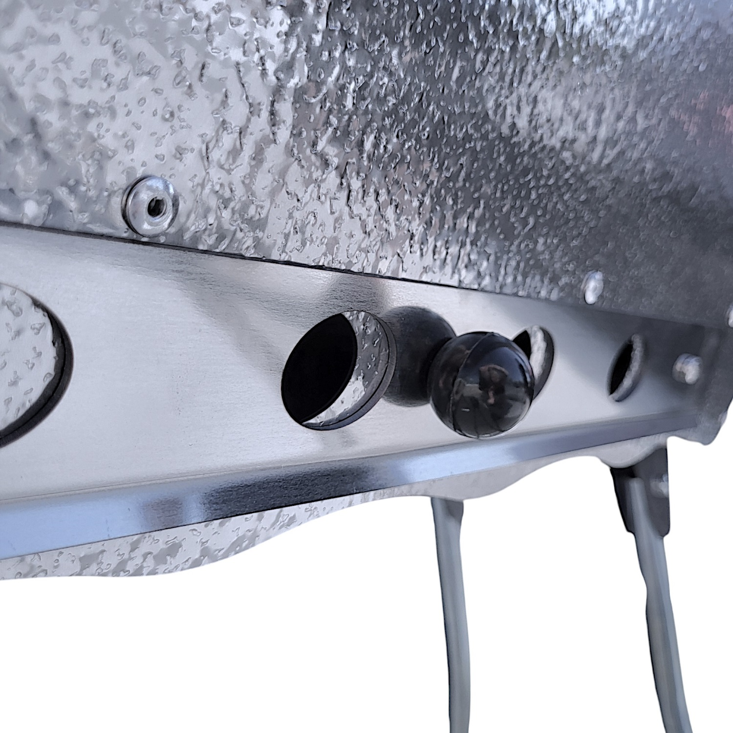 Nahaufnahme eines Metallgrills mit ovalen Löchern und einem schwarzen Knopf.