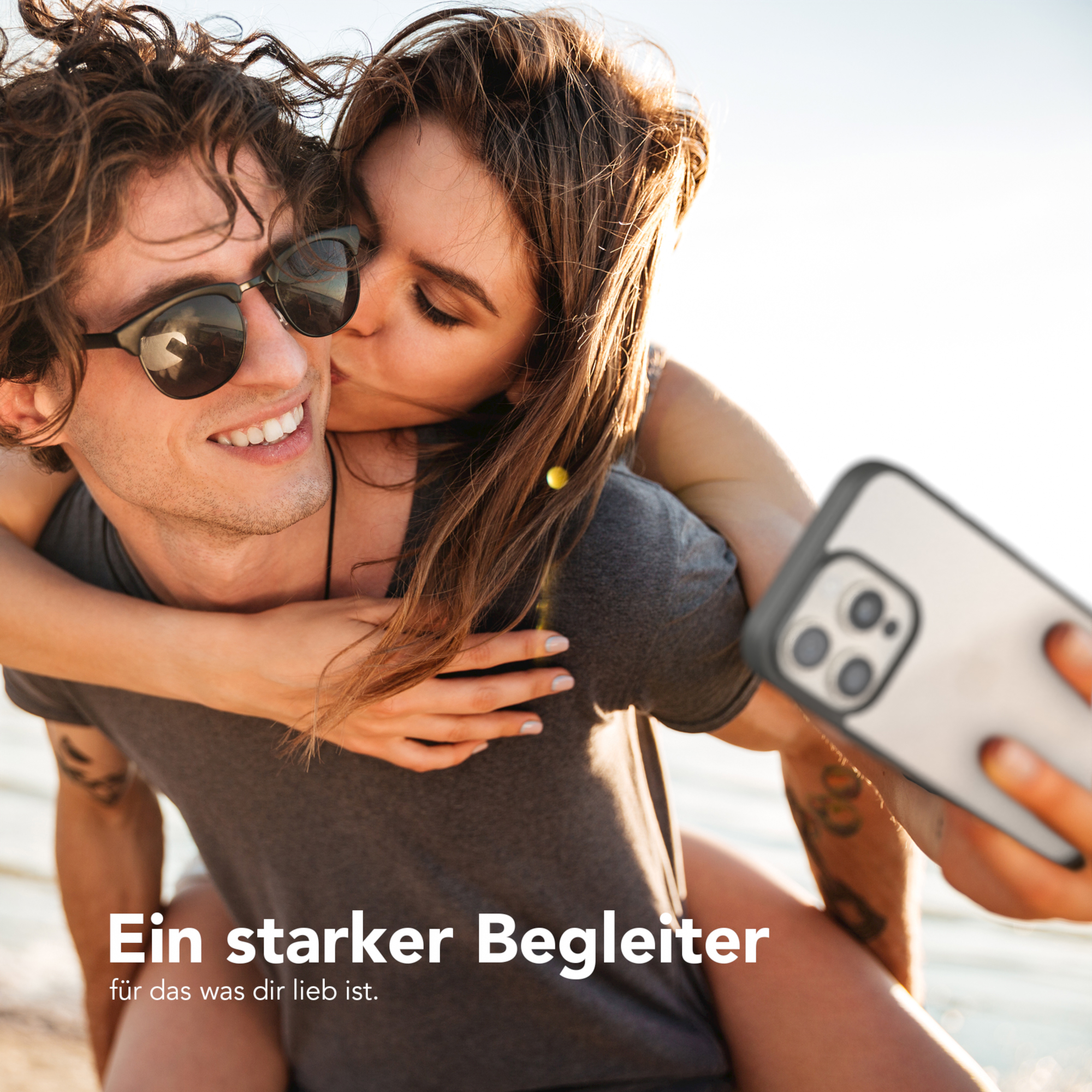 Ein Paar macht ein Selfie. Die Frau küsst den Mann. Das Telefon ist im Bild.