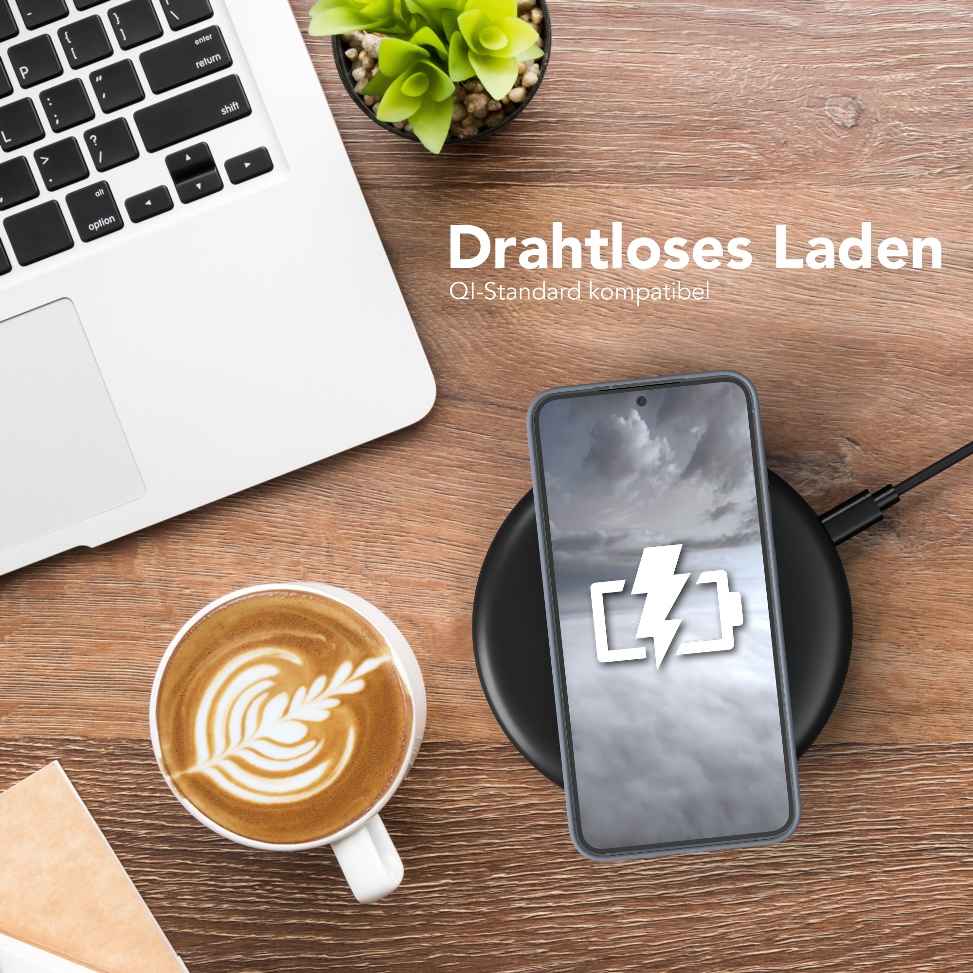 Ein Laptop, ein drahtlos geladenes Telefon, Kaffee und eine Pflanze auf einem Holztisch.