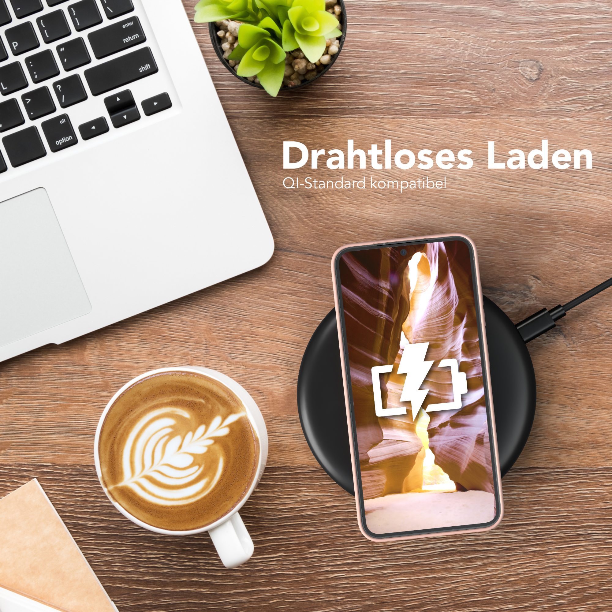 Ein Telefon, das drahtlos auf einem schwarzen Pad geladen wird, neben einem Laptop und einer Tasse Kaffee. Draufsicht.