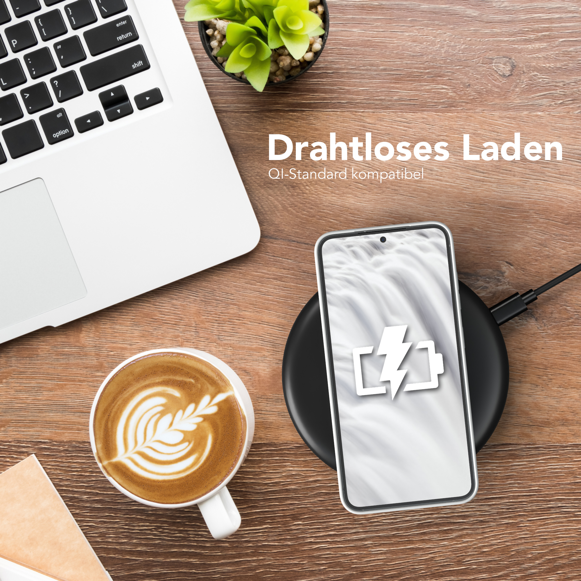 Telefon lädt drahtlos auf einem Pad. Laptop und Kaffee sichtbar. Hintergrund: Holztisch.