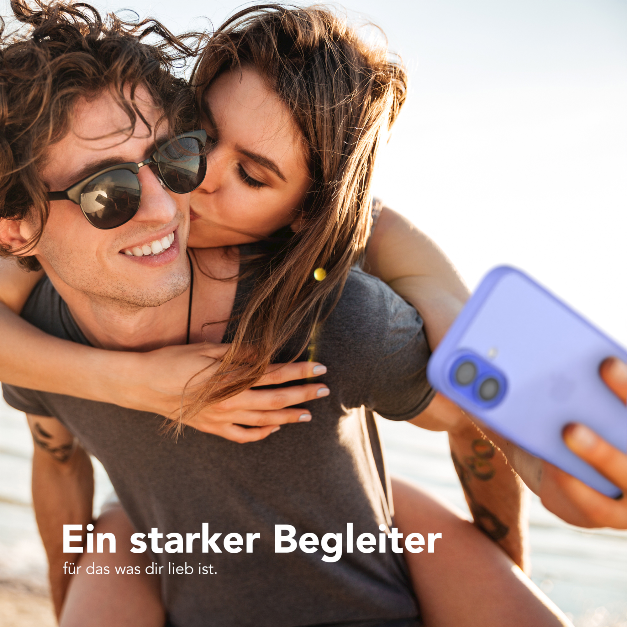 Ein Paar macht ein Selfie, die Frau küsst die Wange des Mannes. Sie halten ein Telefon.