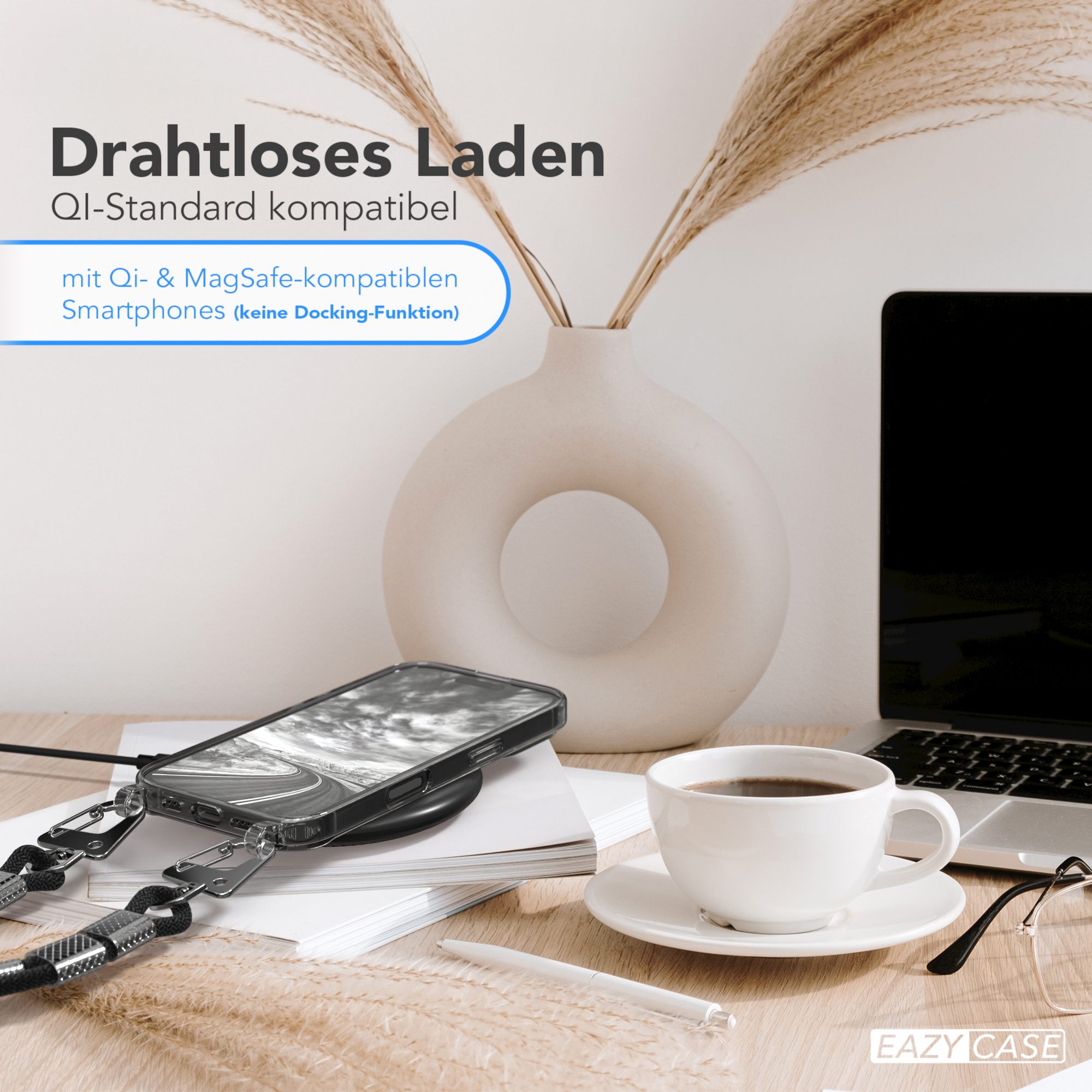 Telefon auf kabellosem Ladegerät, Kaffeetasse und Brille. Pampasgras und Laptop im Hintergrund.