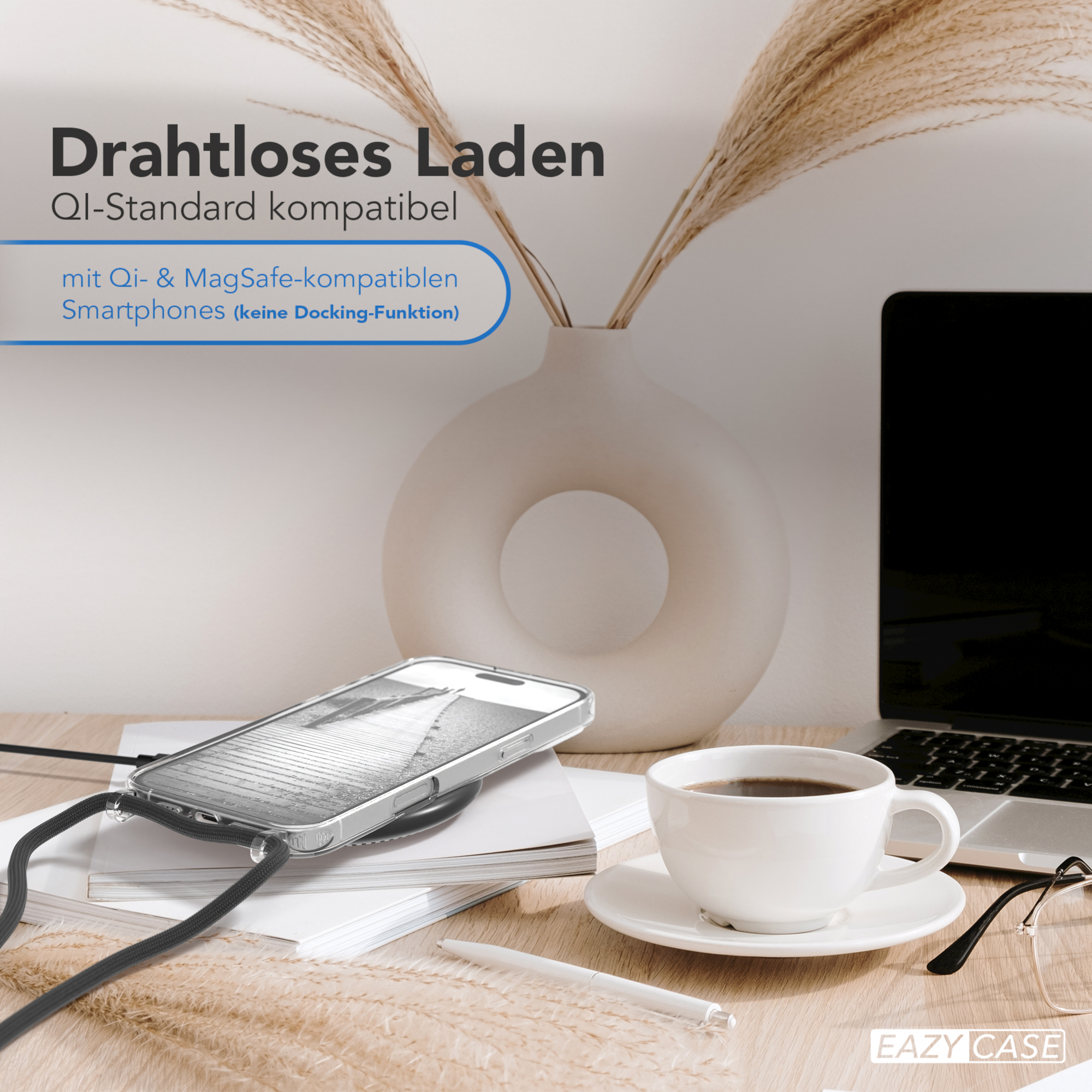 Telefon auf kabellosem Ladegerät. Weiße Vase mit Pflanzen, Kaffeetasse und Laptop auf Holztisch.