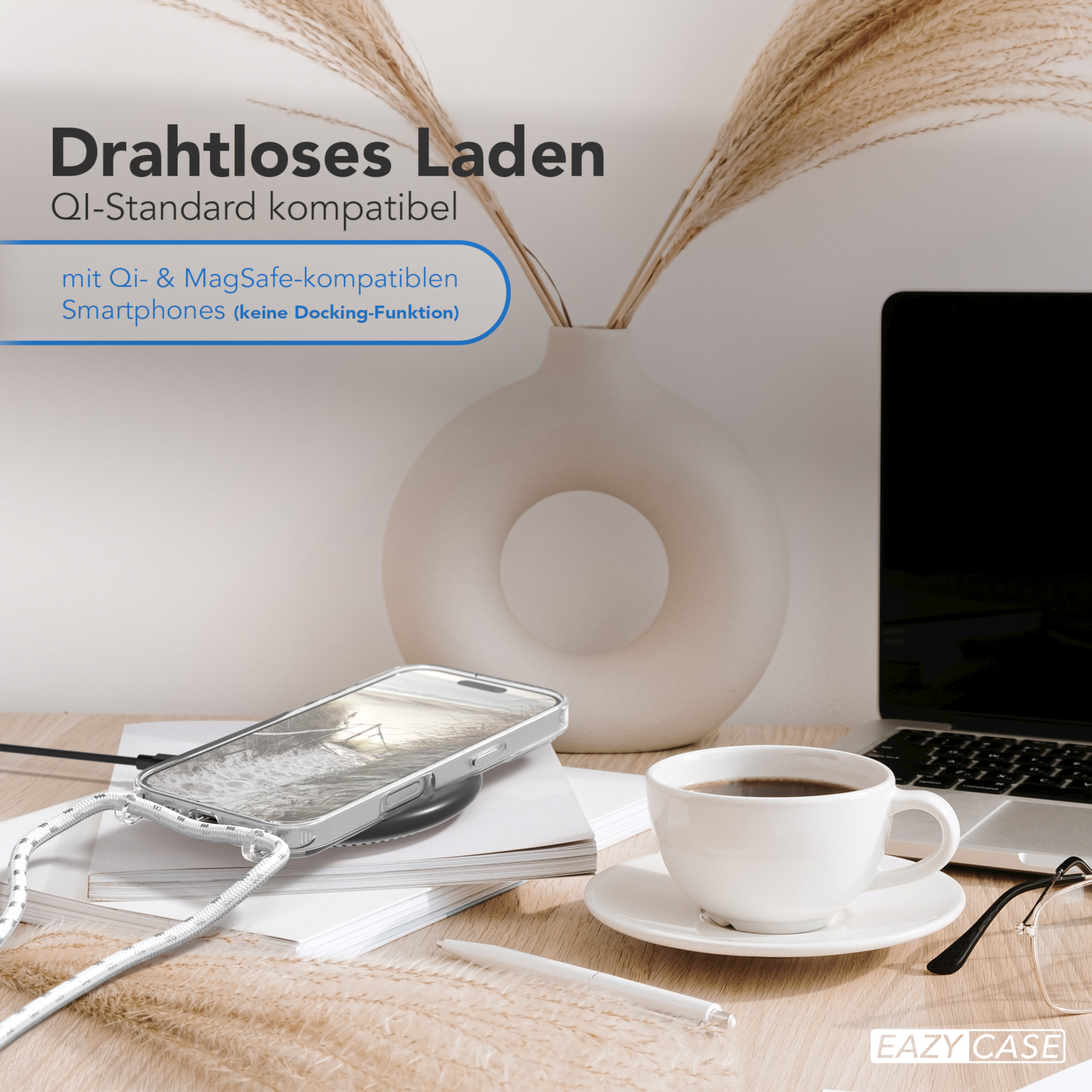 Telefon wird kabellos auf einem Tisch aufgeladen. Vase, Kaffeetasse und Laptop sind vorhanden.