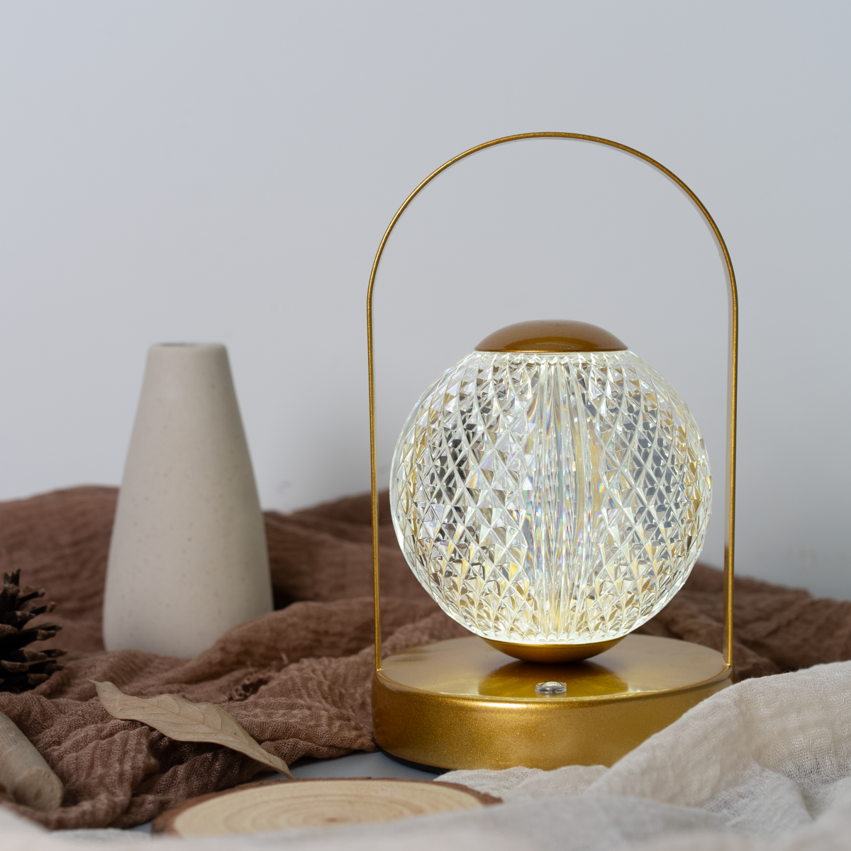 Una lámpara dorada con una pantalla de bola de cristal sobre una mesa, con un jarrón y piña.