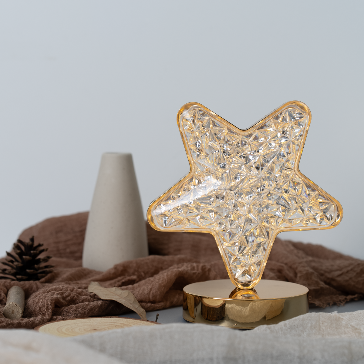 Lámpara en forma de estrella con base dorada sobre mesa decorada.