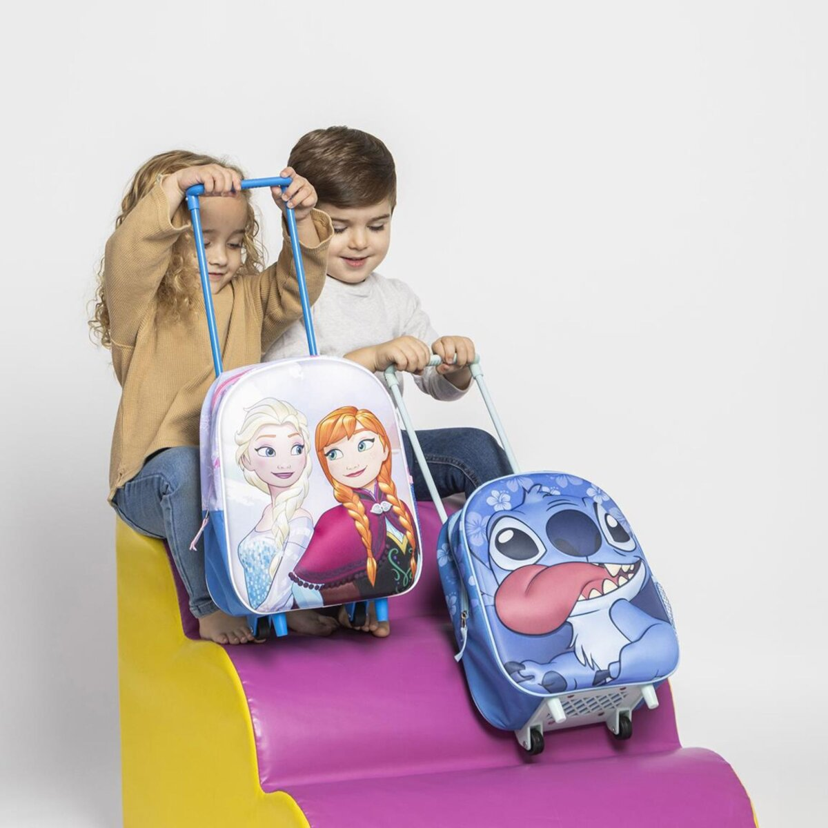 Zwei Kinder ziehen Gepäck mit Zeichentrickfiguren darauf. Eines ist Elsa und Anna.
