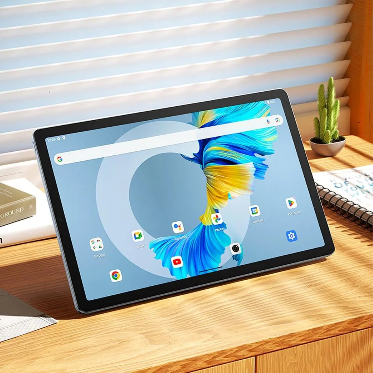 Un tablet con uno sfondo astratto colorato è appoggiato su una scrivania di legno vicino a libri e un cactus.