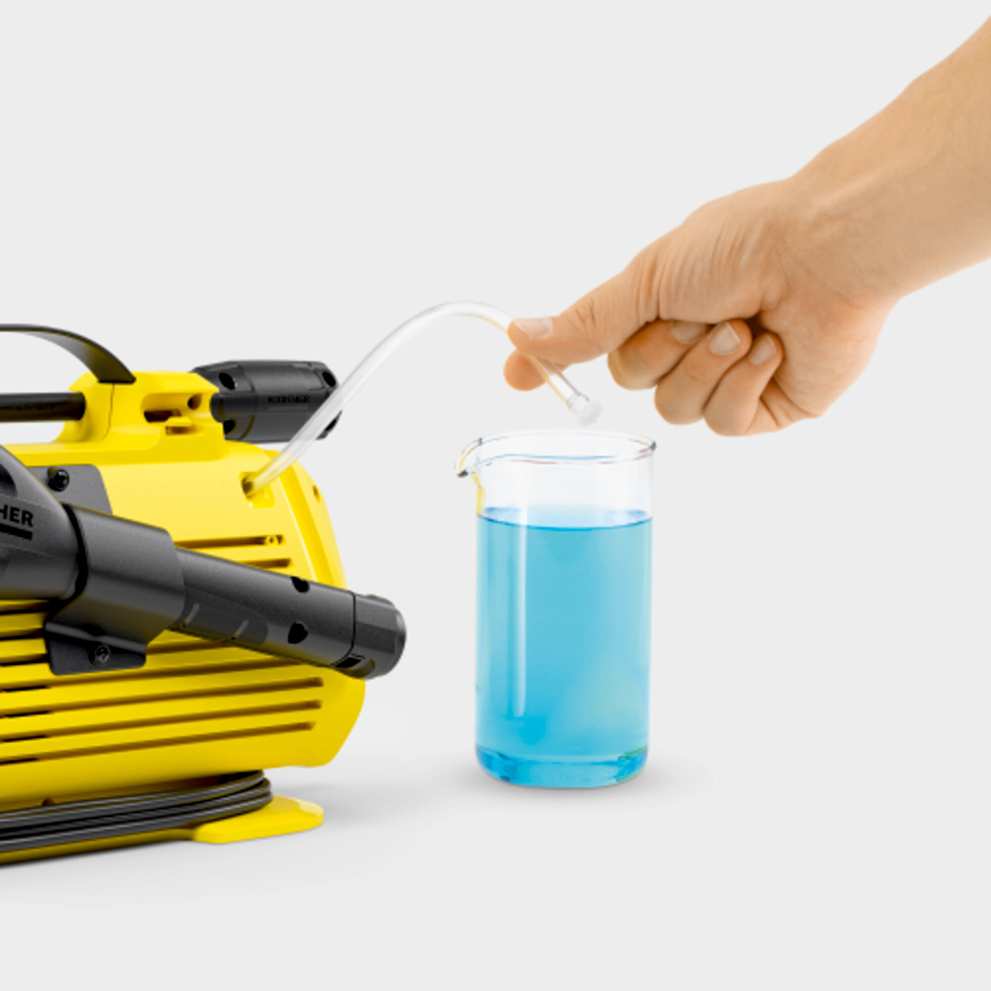 Eine Hand gießt blaue Flüssigkeit in einen Glasbecher, mit gelber Maschine.