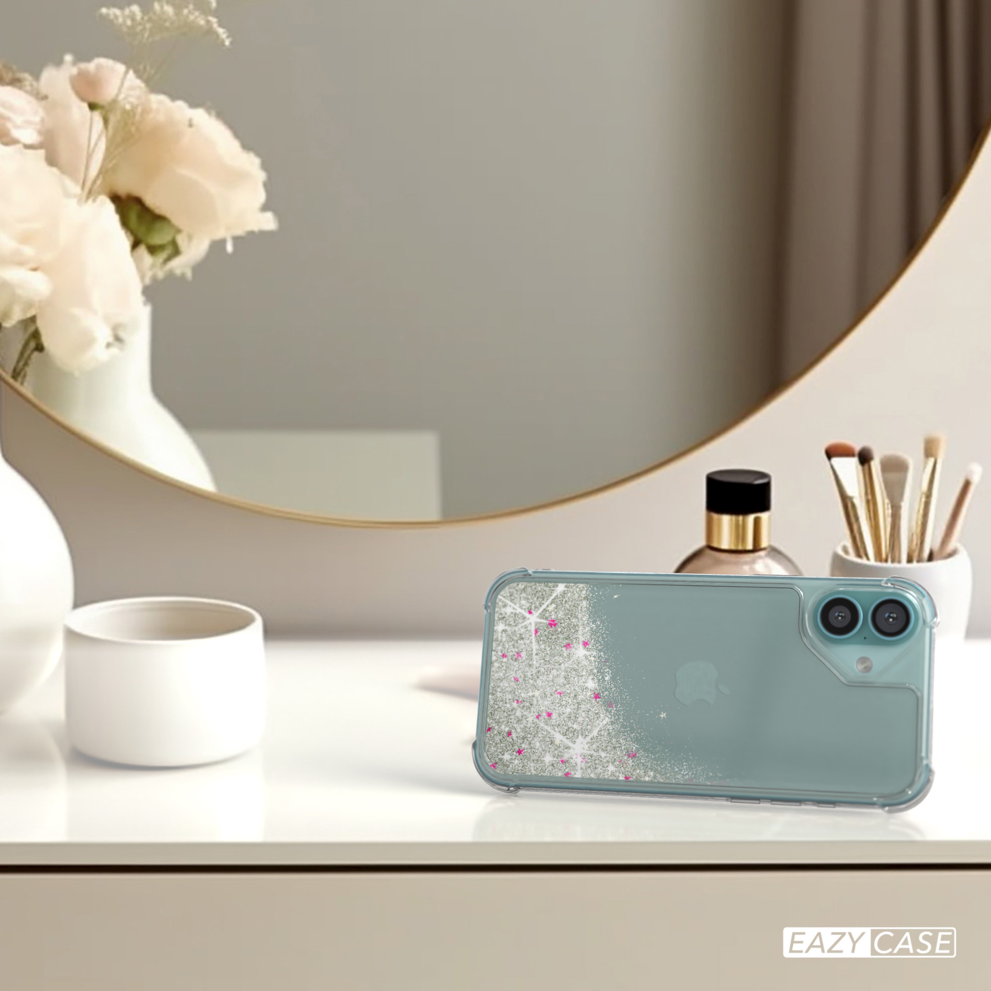Eine Handyhülle mit Glitzer auf einem weißen Tisch. Blumen und ein Spiegel im Hintergrund.
