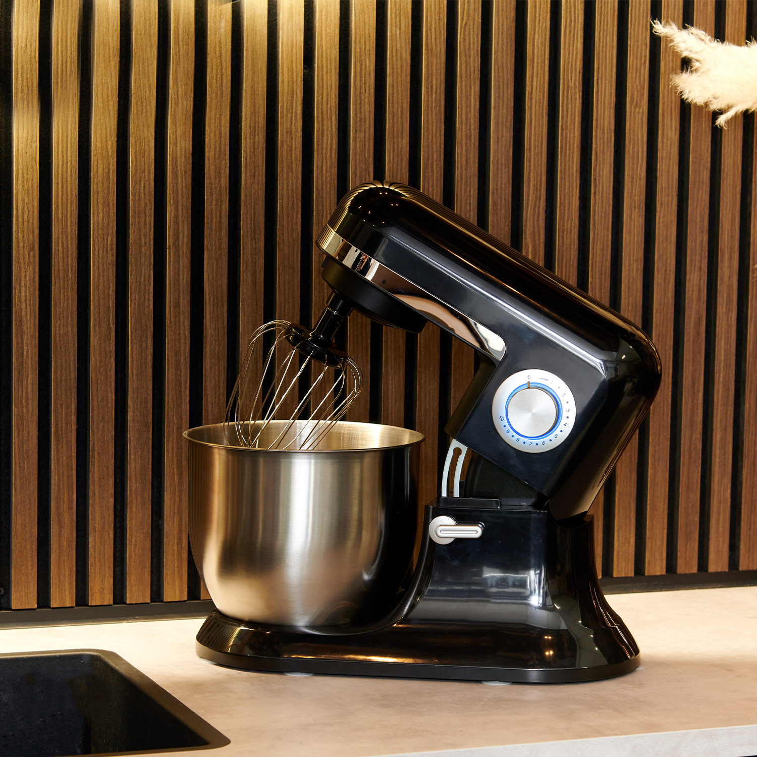 Black kitchen mixer, stainless steel bowl, and a wooden background.