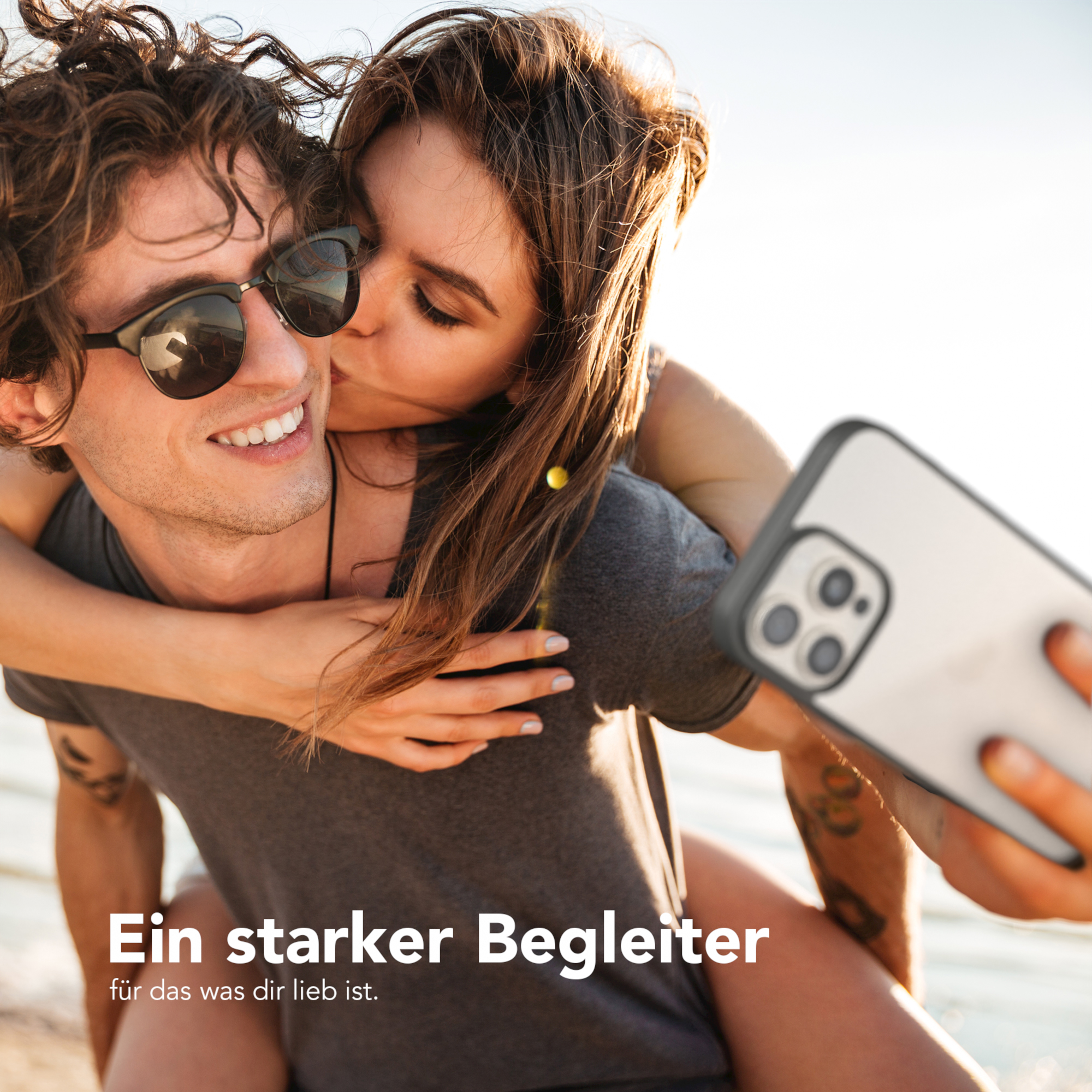 Frau küsst Mann mit Sonnenbrille; sie machen ein Selfie. Strandszene.