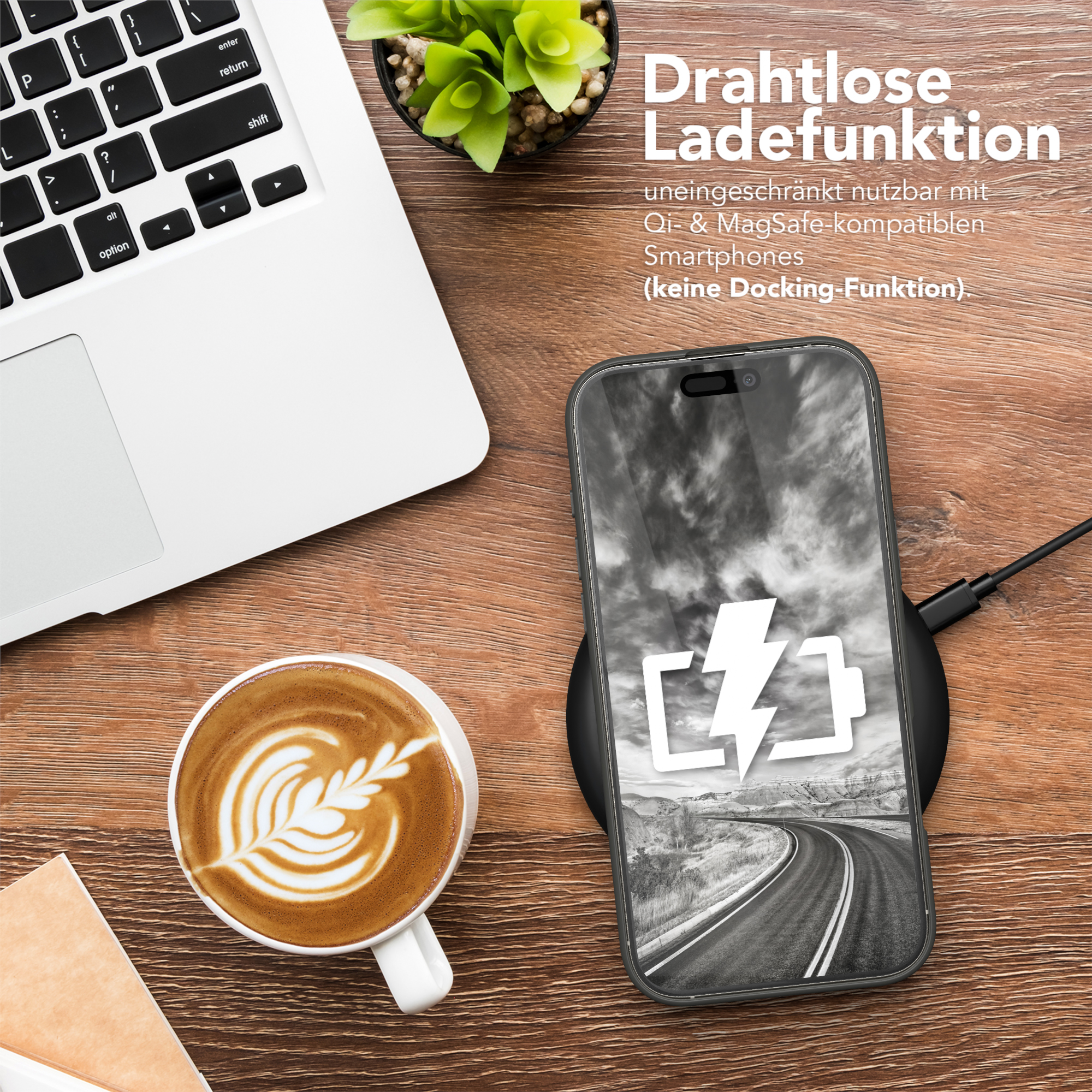 Ein Telefon, das auf einem Pad geladen wird, mit einer Kaffeetasse und einem Laptop auf einem Holztisch.