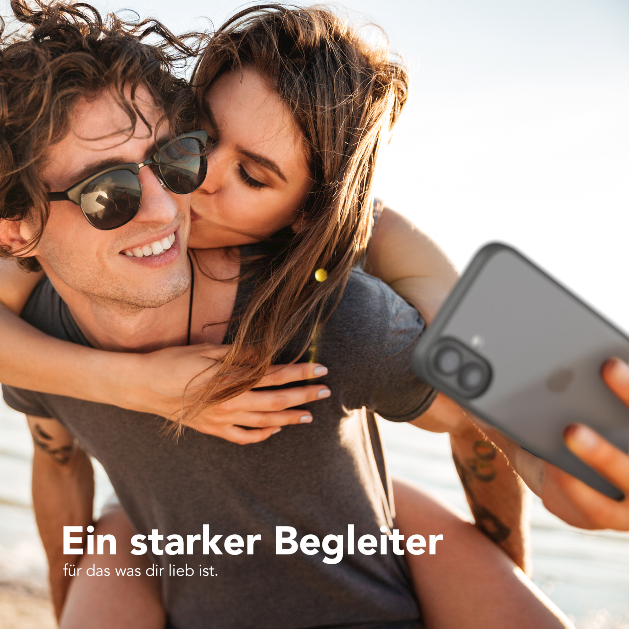 Paar macht ein Selfie. Die Frau küsst den Mann auf die Wange. Telefon ist im Bild.