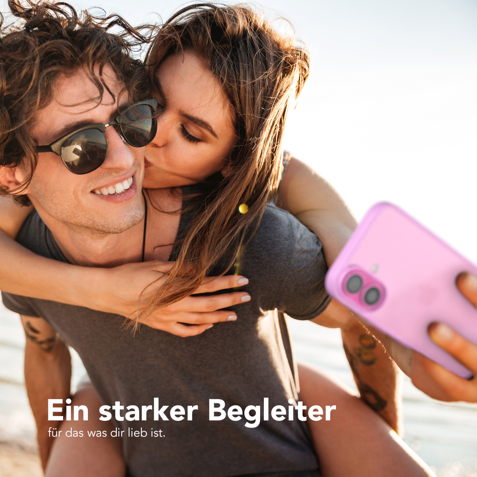 Ein Mann umarmt und küsst eine Frau. Sie lächeln, während sie ein Selfie mit einem rosa Telefon machen.