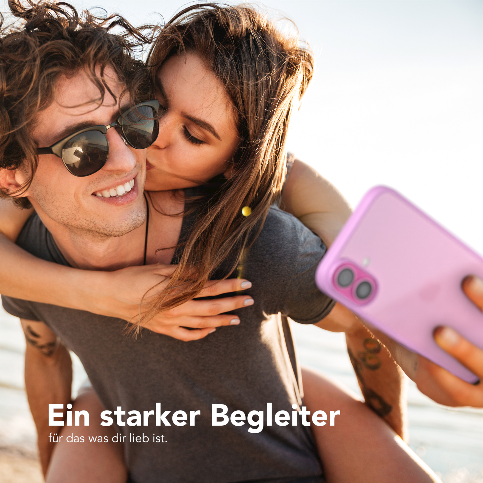 Ein Paar macht ein Selfie mit einer rosa Handyhülle. Die Frau küsst den Mann auf die Wange.