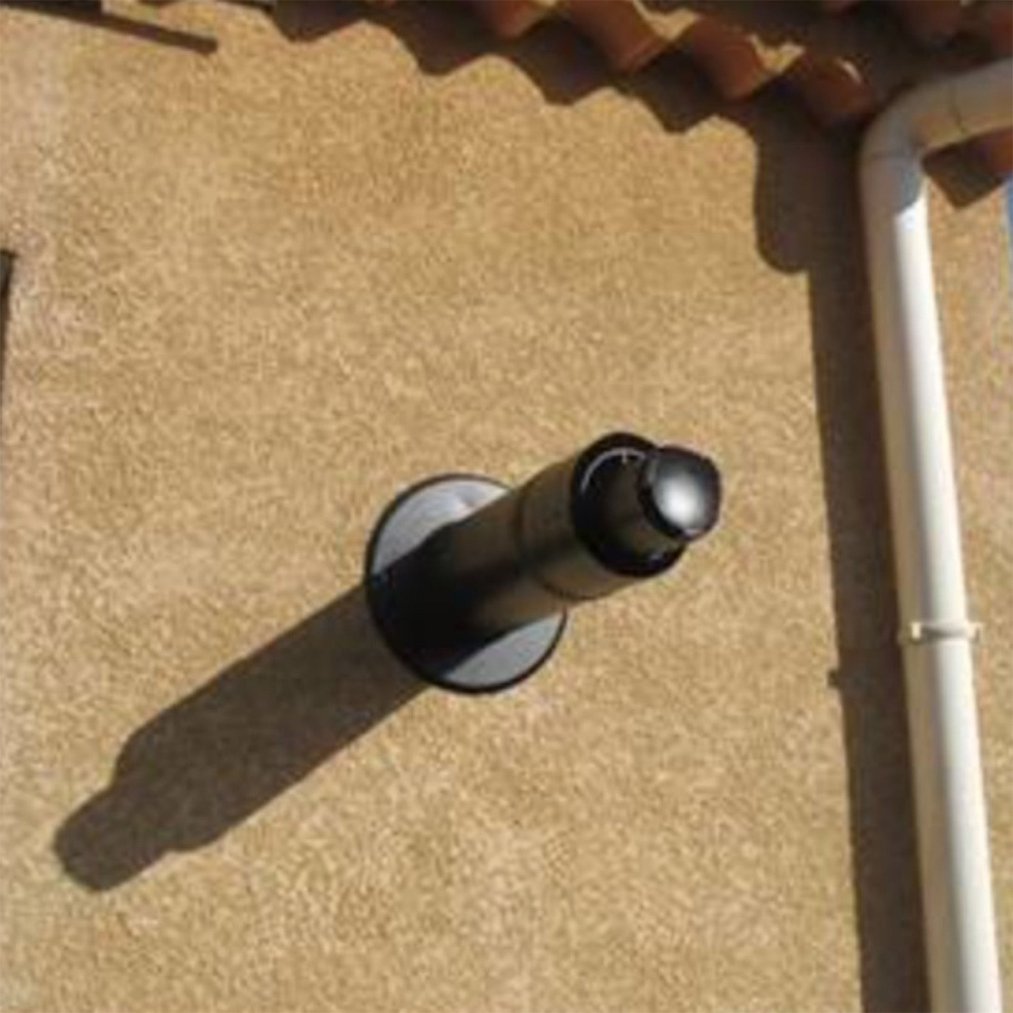Una tubería negra en una pared beige. La tubería tiene un extremo curvo y una sombra.