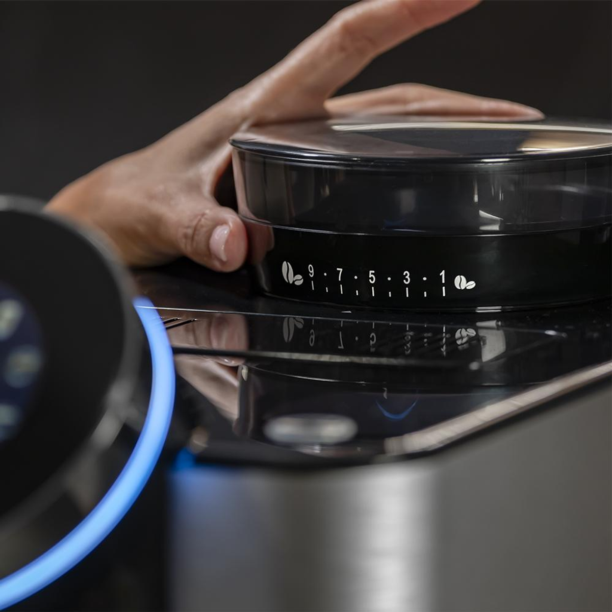 Zbliżenie dłoni regulującej pokrętło ustawień ekspresu do kawy. Czarna powierzchnia z ikonami ziaren kawy.