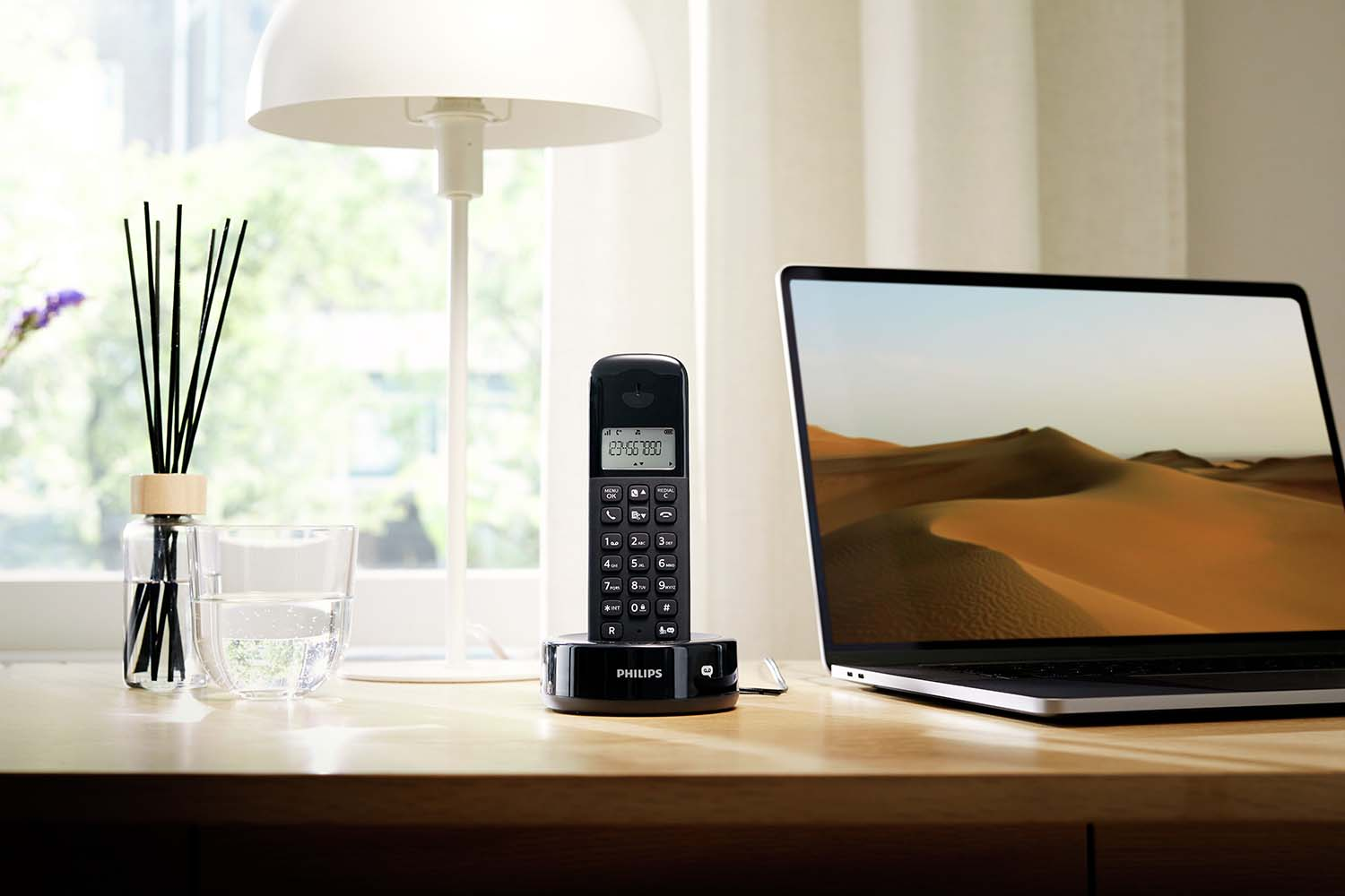 Téléphone fixe noir avec socle et lampe sur un bureau avec ordinateur portable.