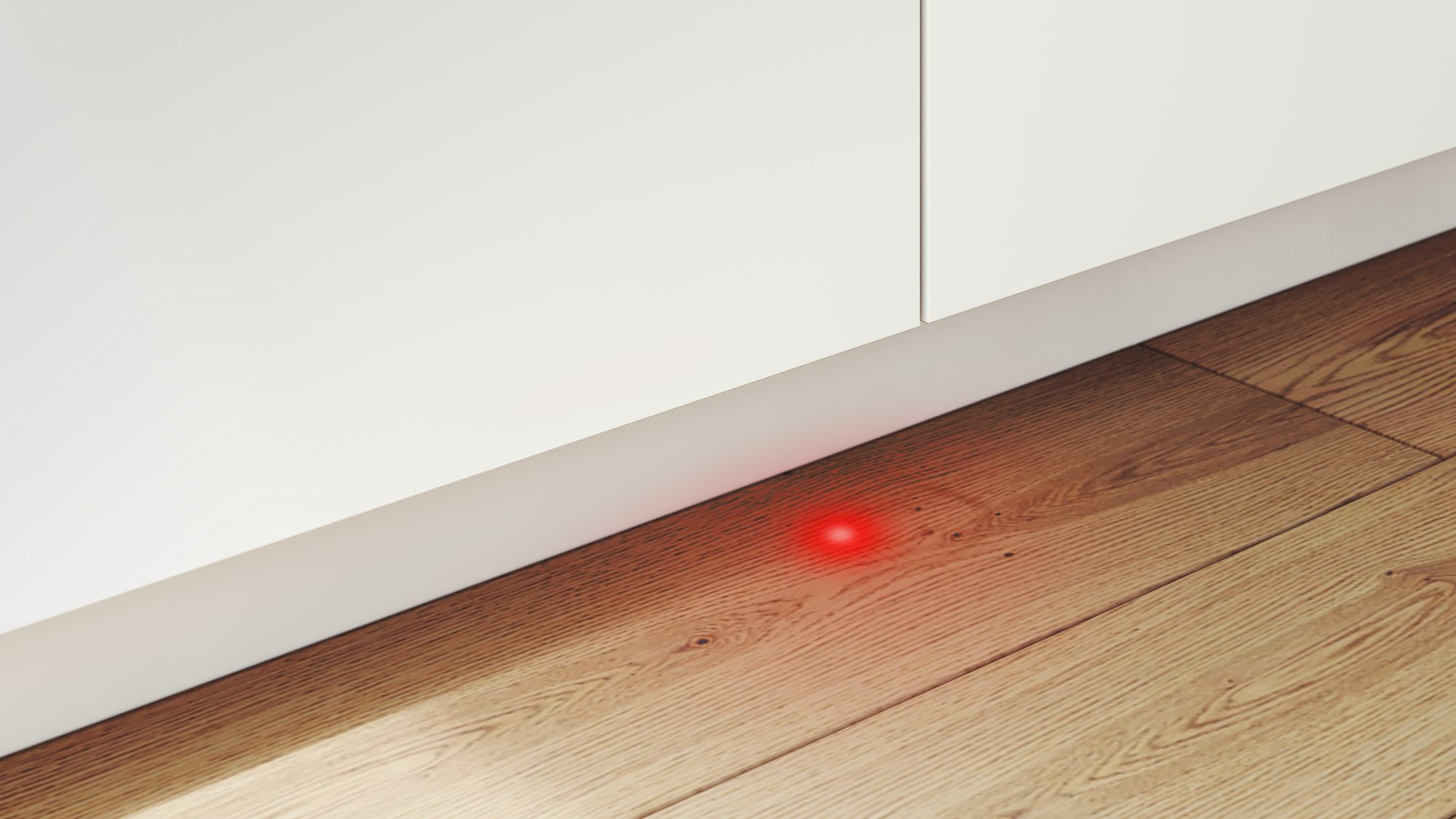 Rotes Licht auf einem Holzboden, in der Nähe eines weißen Schrankfußes.