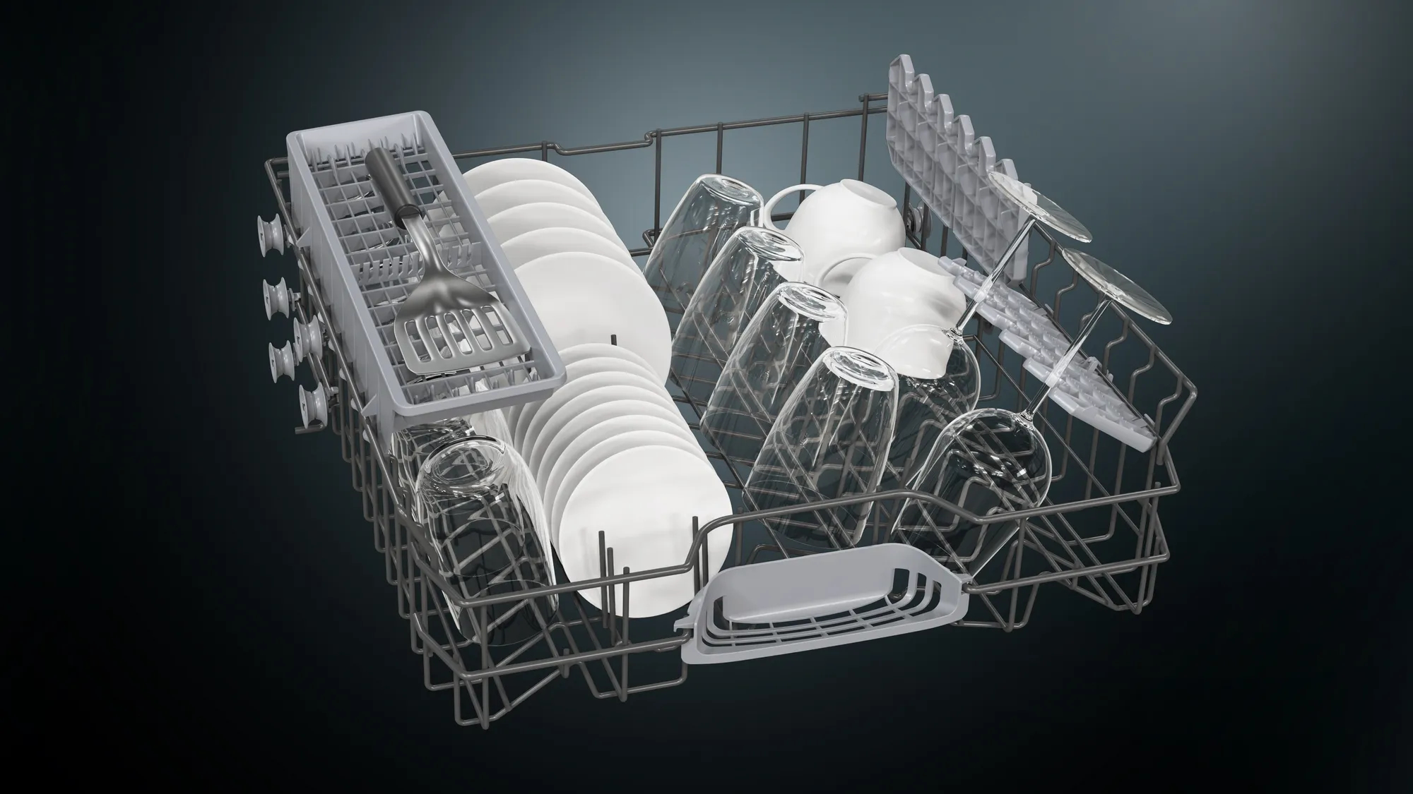 Kosz zmywarki wypełniony naczyniami, szklankami i sztućcami na ciemnym tle.