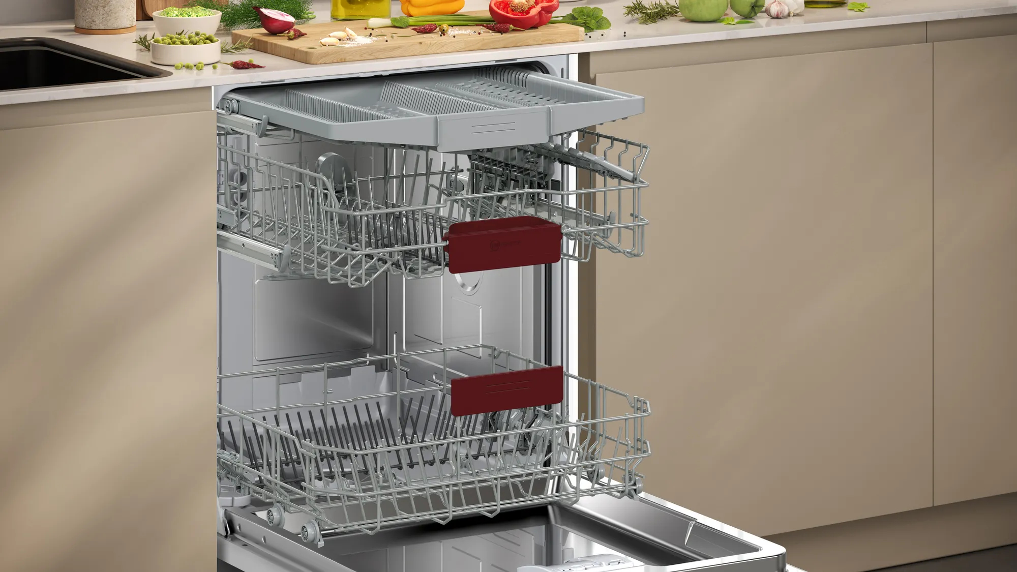 Lavastoviglie con cestelli, blocchi rossi. Utensili e piatti visibili. Cucina beige e bianca.