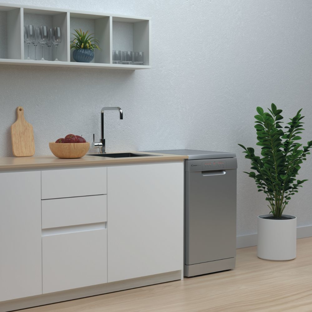 Escena de cocina con lavavajillas, fregadero y planta. Manzanas rojas en un cuenco sobre encimera.