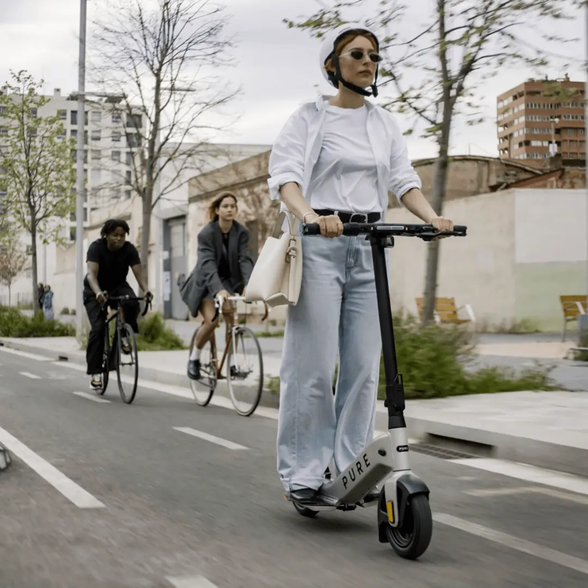 Frau auf Elektroroller, andere Leute auf Fahrrädern. Urbanes Umfeld. Sonniger Tag.