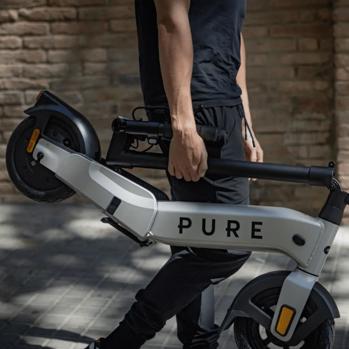 Eine Person trägt einen grau-schwarzen Elektroroller. Auf dem Roller steht das Wort PURE.