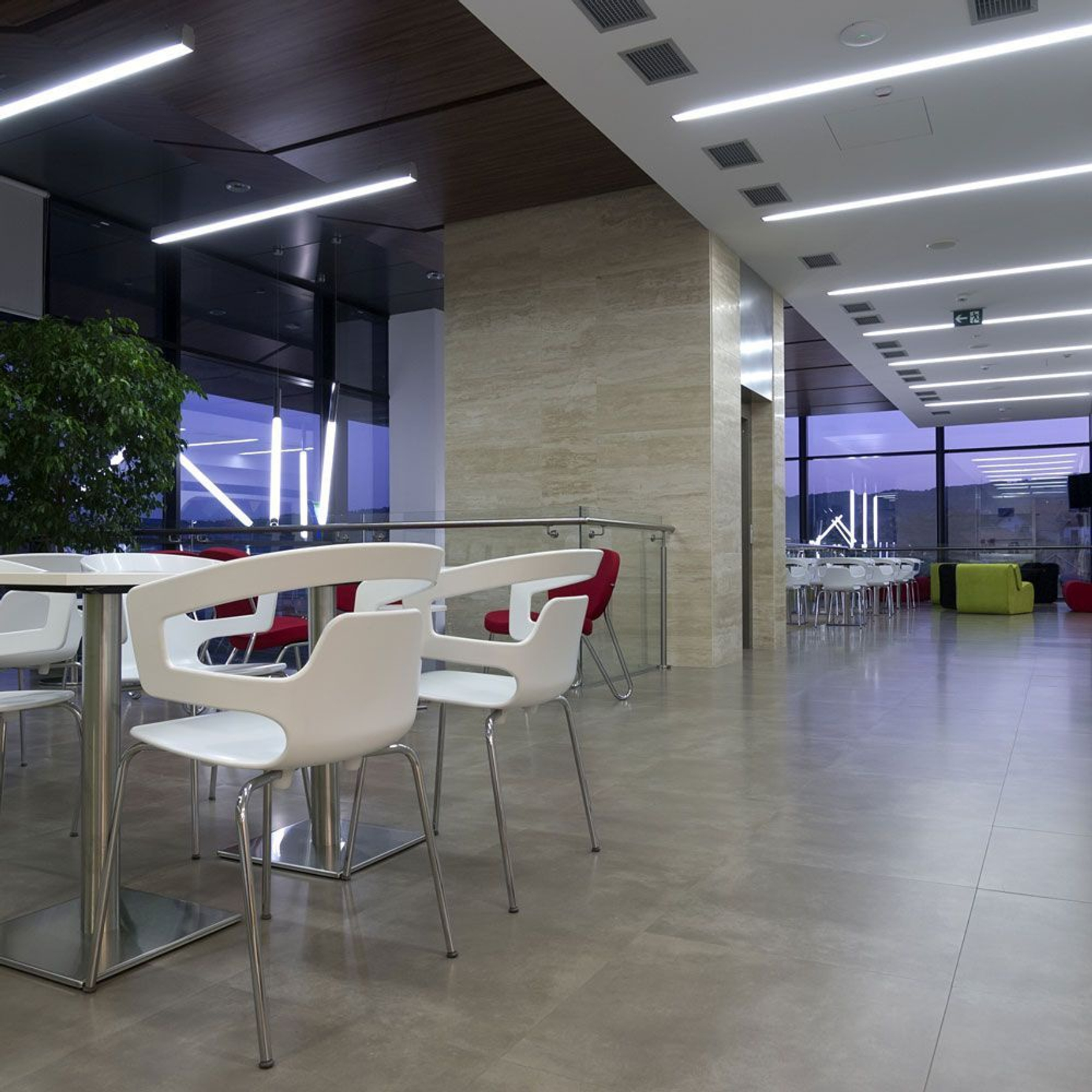 Interni di un ufficio moderno con tavoli, sedie e ampie finestre. Illuminazione brillante e design minimalista.