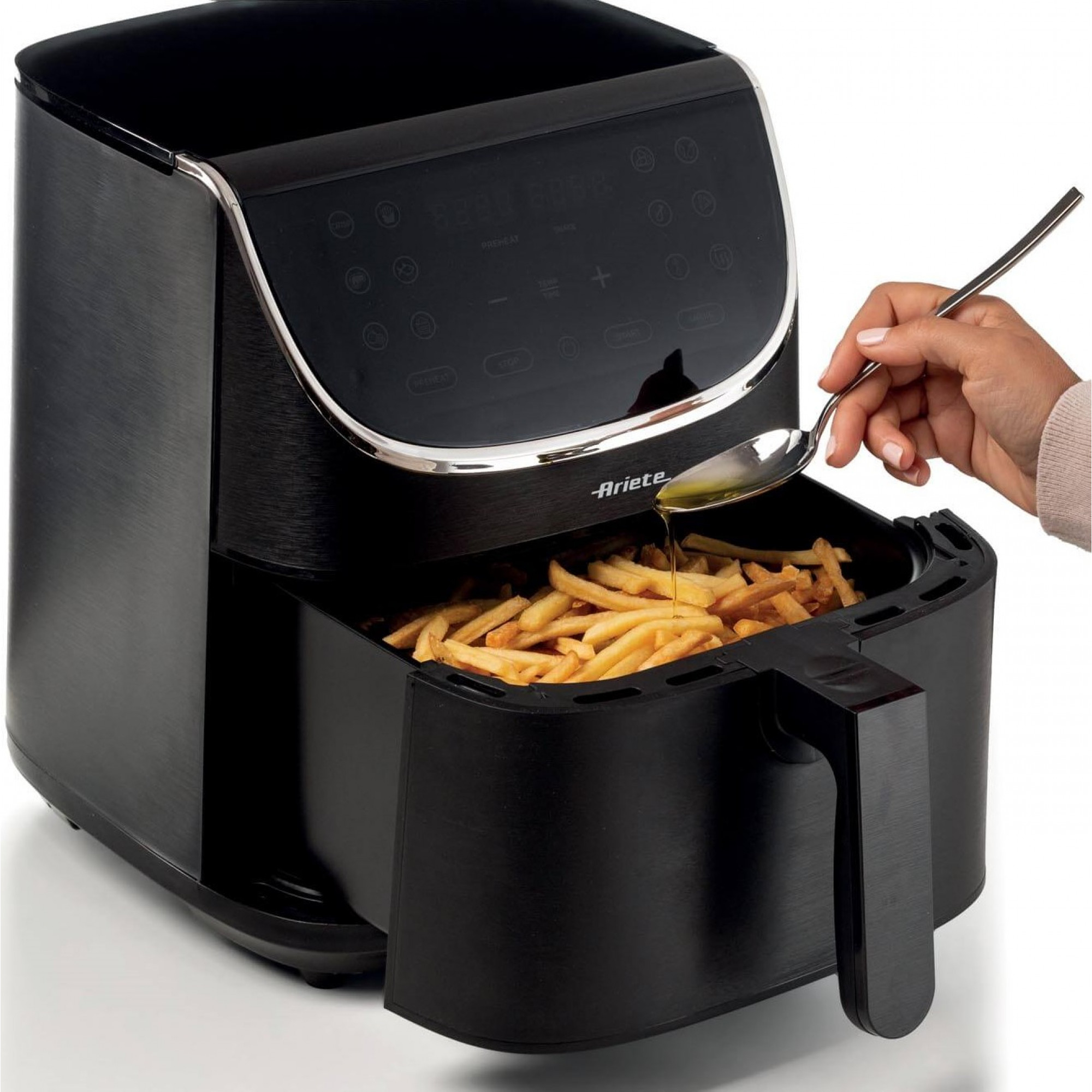 Frytkownica powietrzna z frytkami w środku i ręką wlewającą olej. Czarne urządzenie.