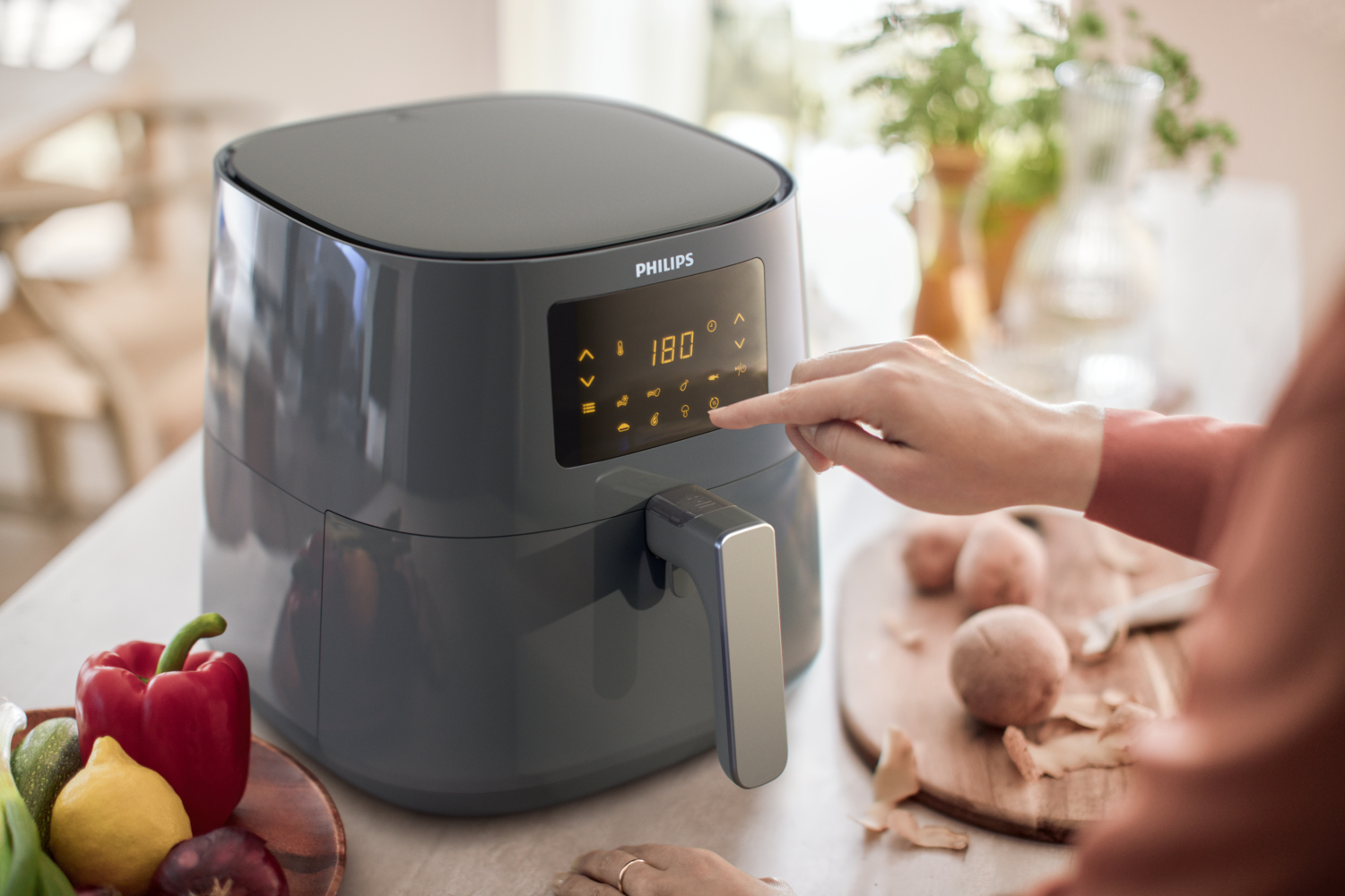 Hand berührt Philips Heißluftfritteuse, Essen und Gemüse daneben.