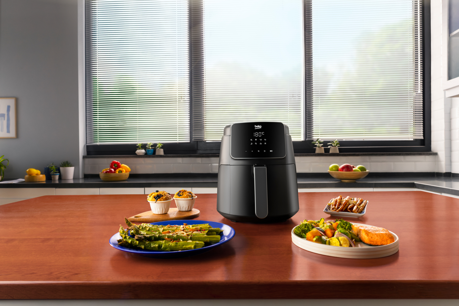 Scena kuchenna z frytkownicą powietrzną na blacie, jedzeniem i oknem z żaluzjami.