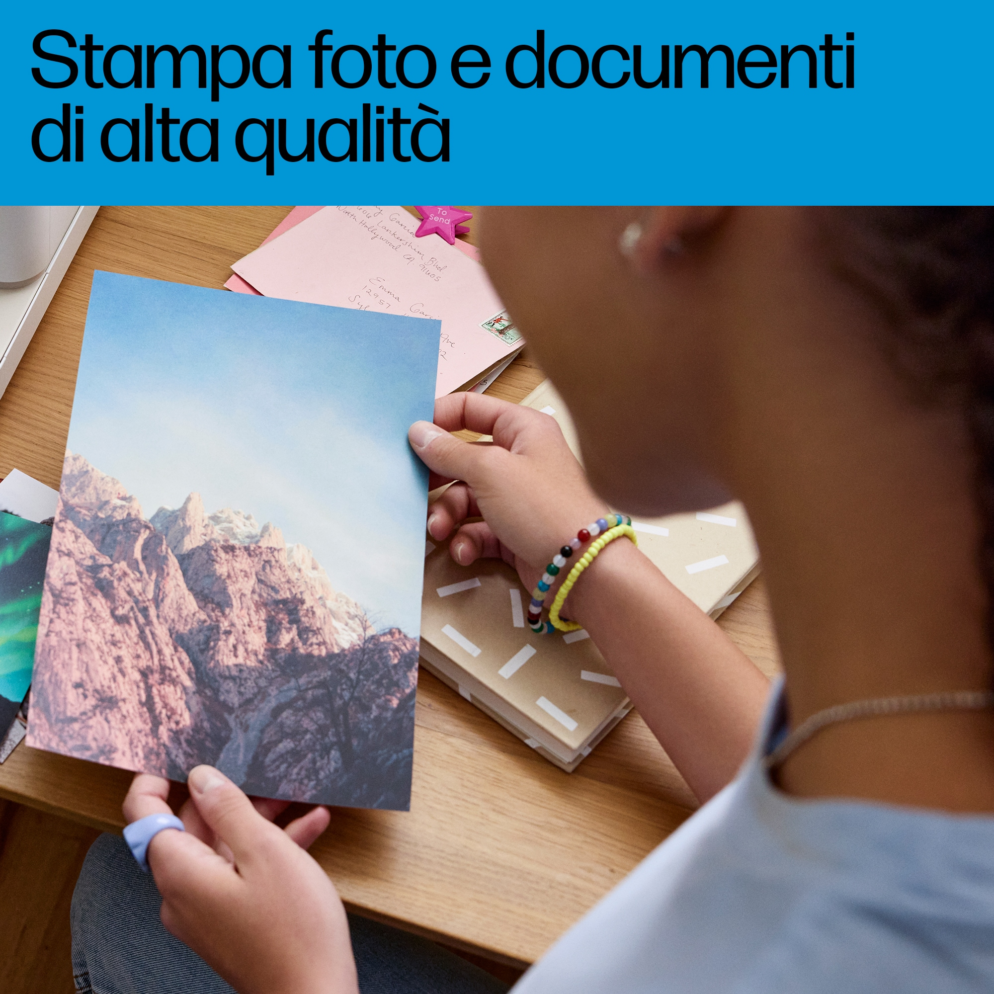 Una persona sostiene una foto de montañas. El texto dice: "Stampa foto e documenti di alta qualità".