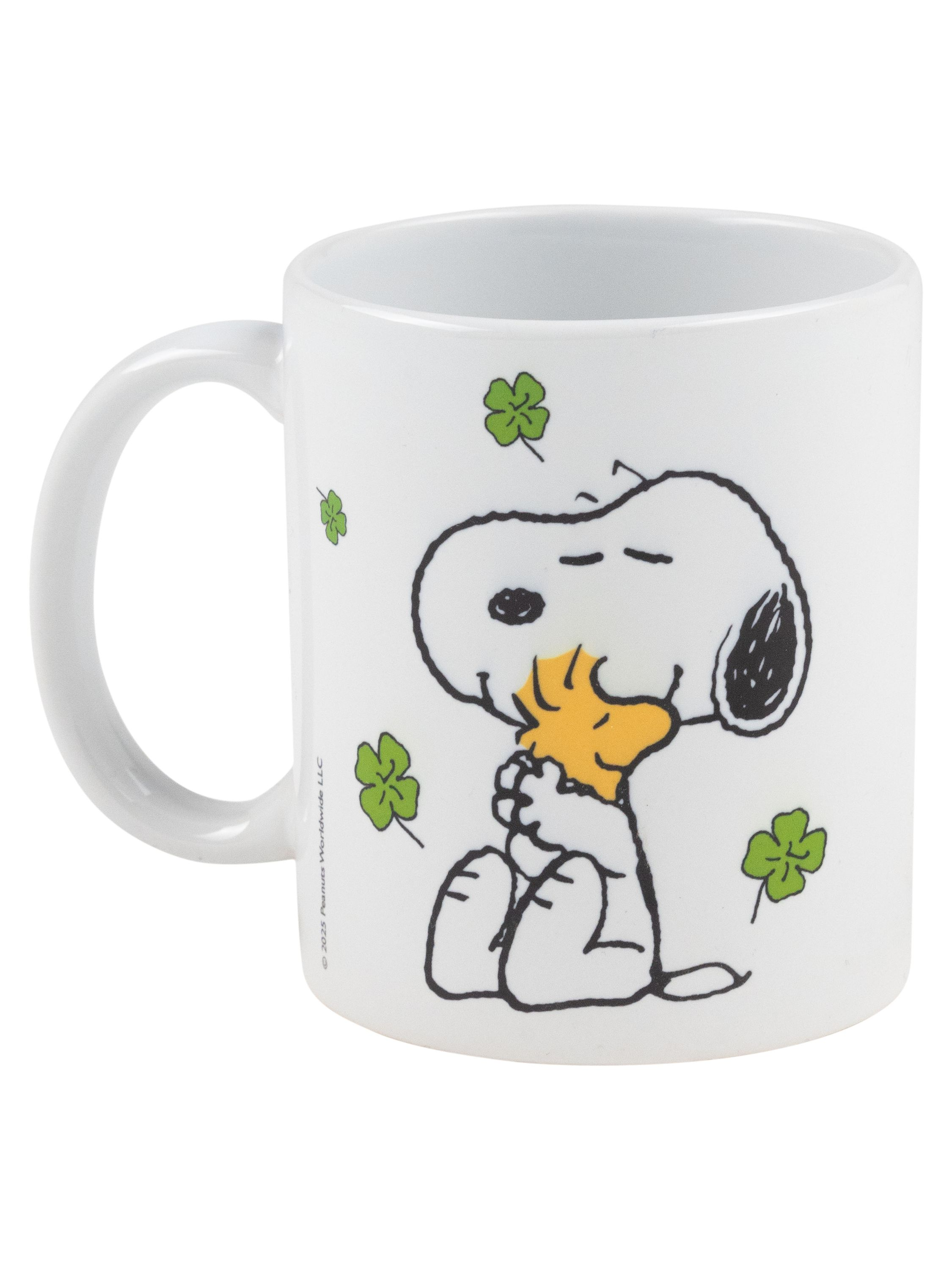 Eine weiße Snoopy-Tasse umarmt Woodstock mit Kleeblättern. Copyright 2023.