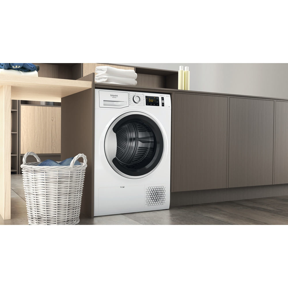 Un'asciugatrice Hotpoint bianca in una lavanderia. C'è un cesto bianco e un bancone in legno.