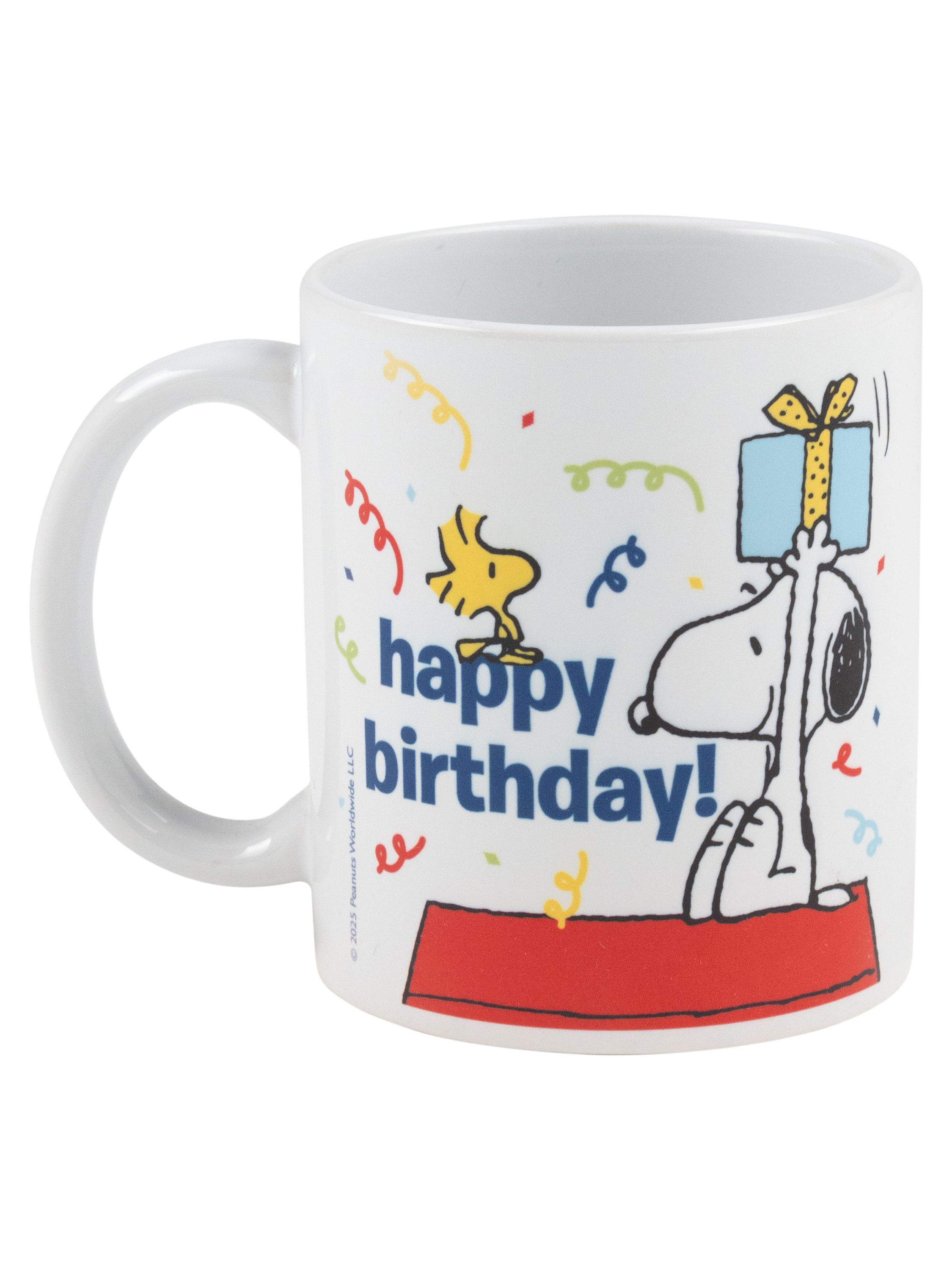 Weiße Tasse mit Snoopy, der ein Geschenk hält, und Woodstock. Alles Gute zum Geburtstag Text. Konfetti im Hintergrund.